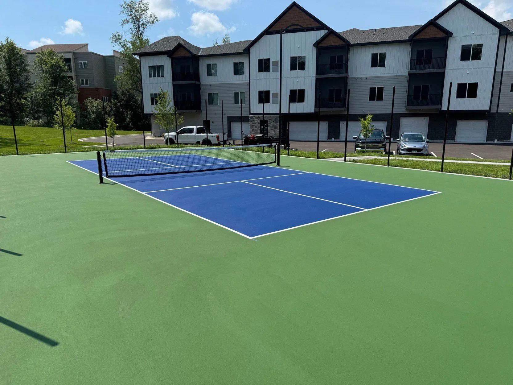 Outdoor blue pickleball court on a green surface in front of apartment buildings