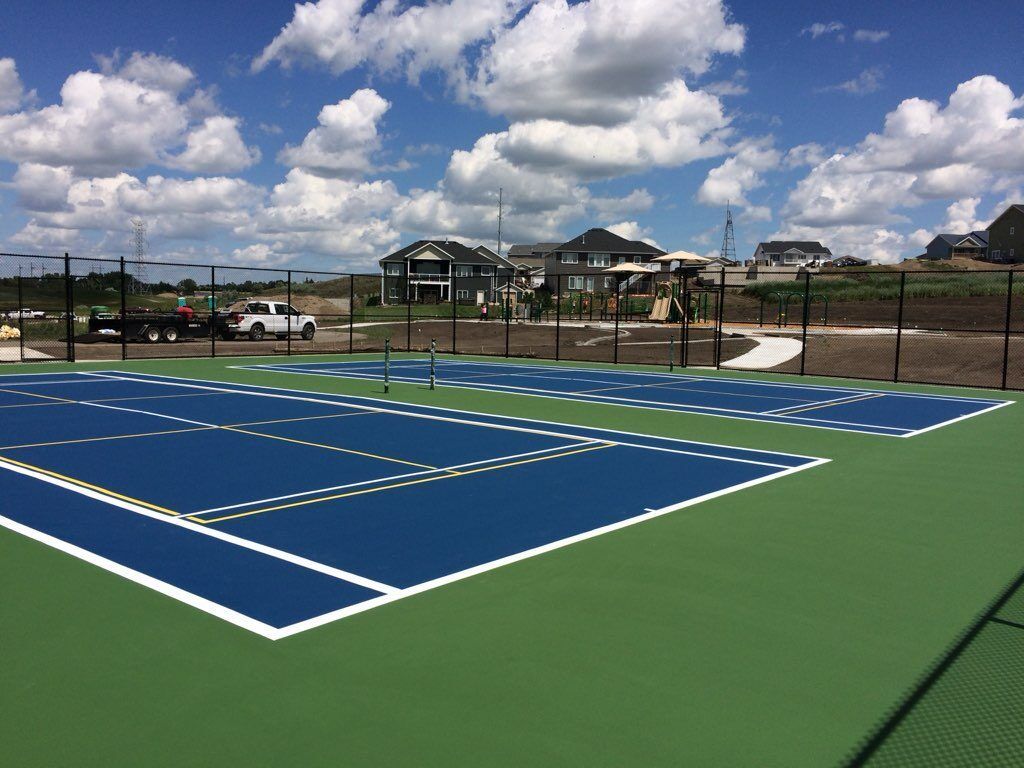 A tennis court with a fence and houses in the background
