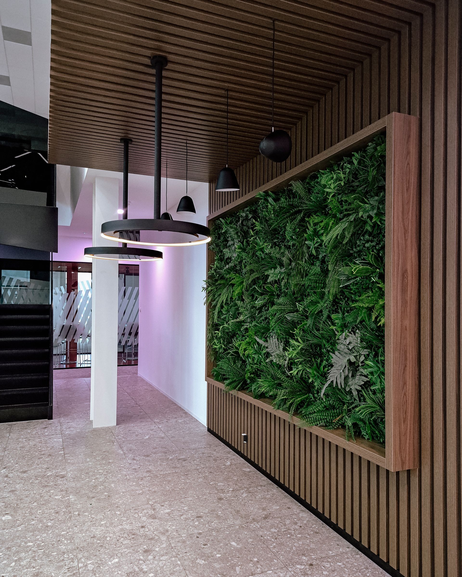 Couloir moderne avec murs lambrissés, luminaires circulaires suspendus et grand mur végétal vertical.