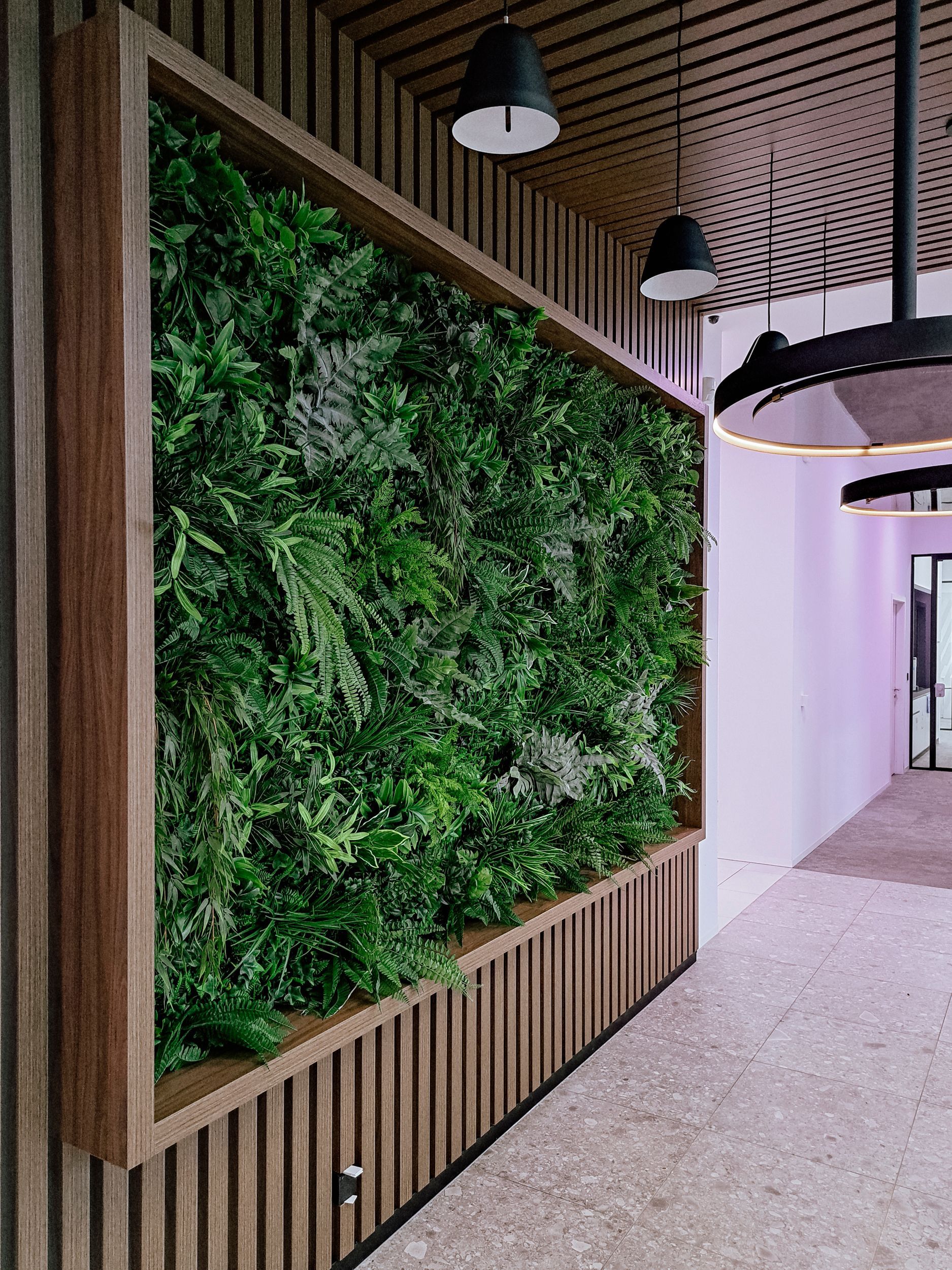 Couloir moderne avec un grand mur végétal, des accents de lattes de bois et des suspensions lumineuses noires.