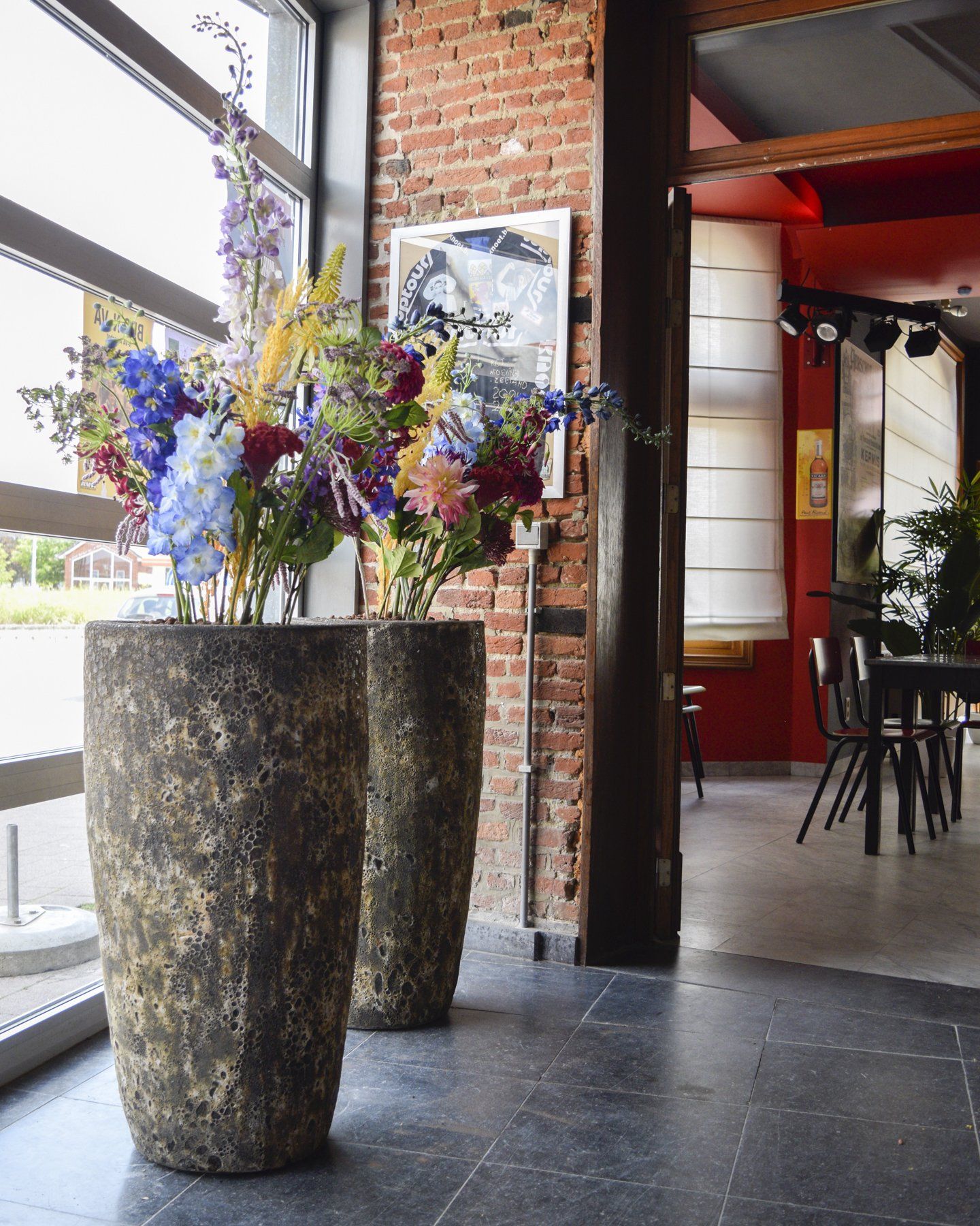 Tall rustic vases filled with colorful flowers in a modern brick-and-glass interior walkway
