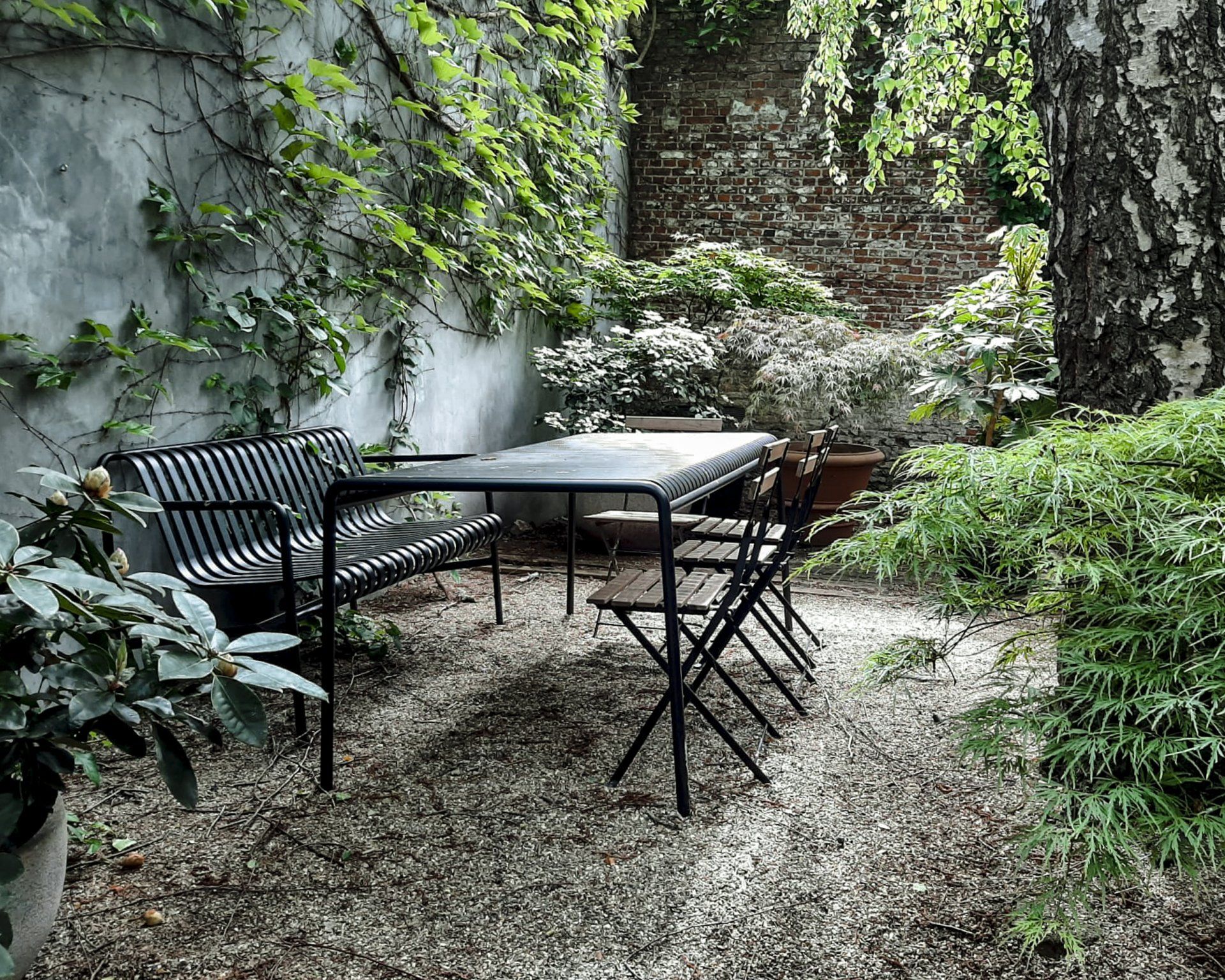Courtyard with black metal table and chairs surrounded by ivy-covered stone walls and greenery