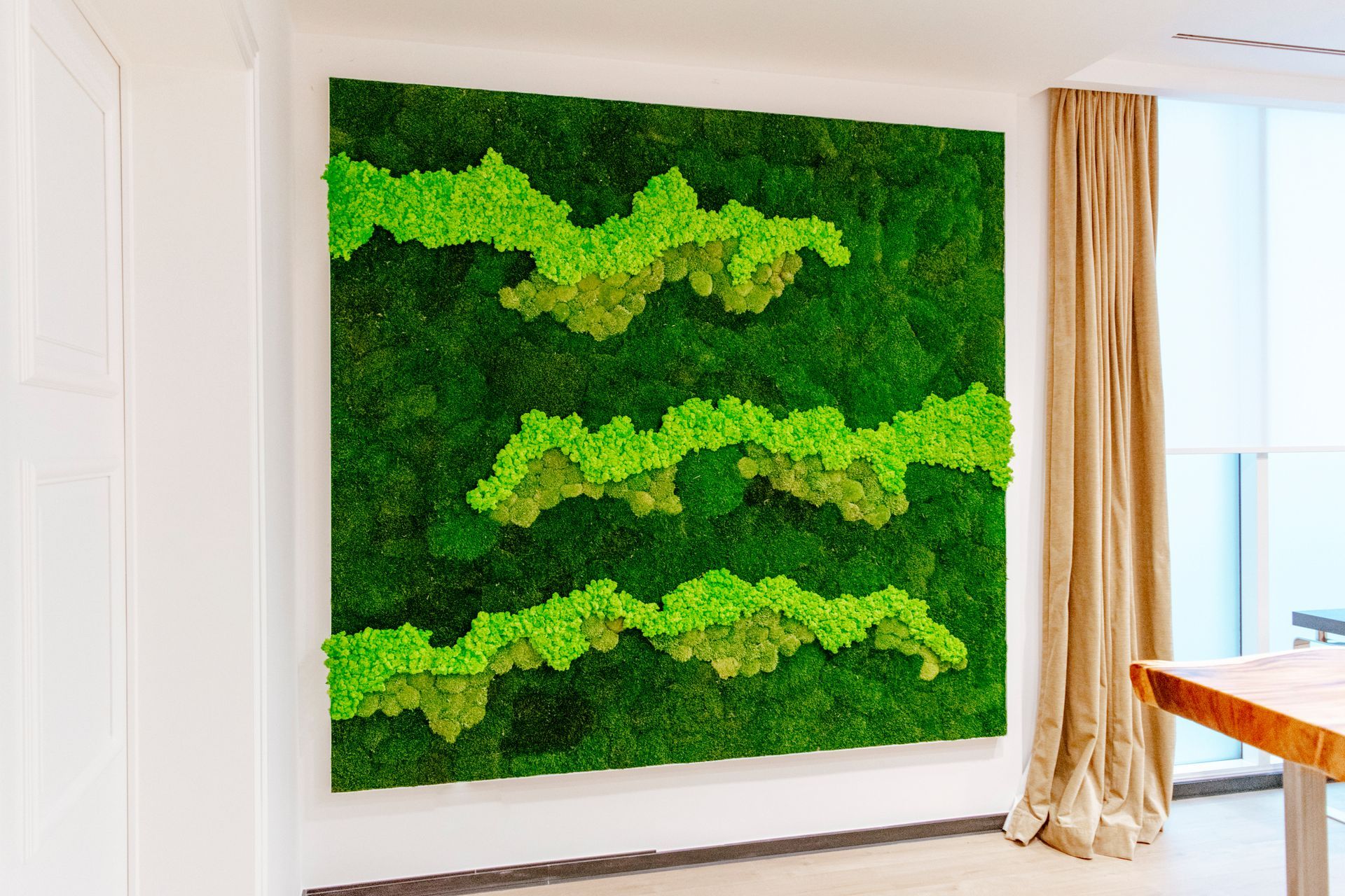 Décoration murale en mousse verte dans une pièce lumineuse, à côté de rideaux beiges et d'une fenêtre