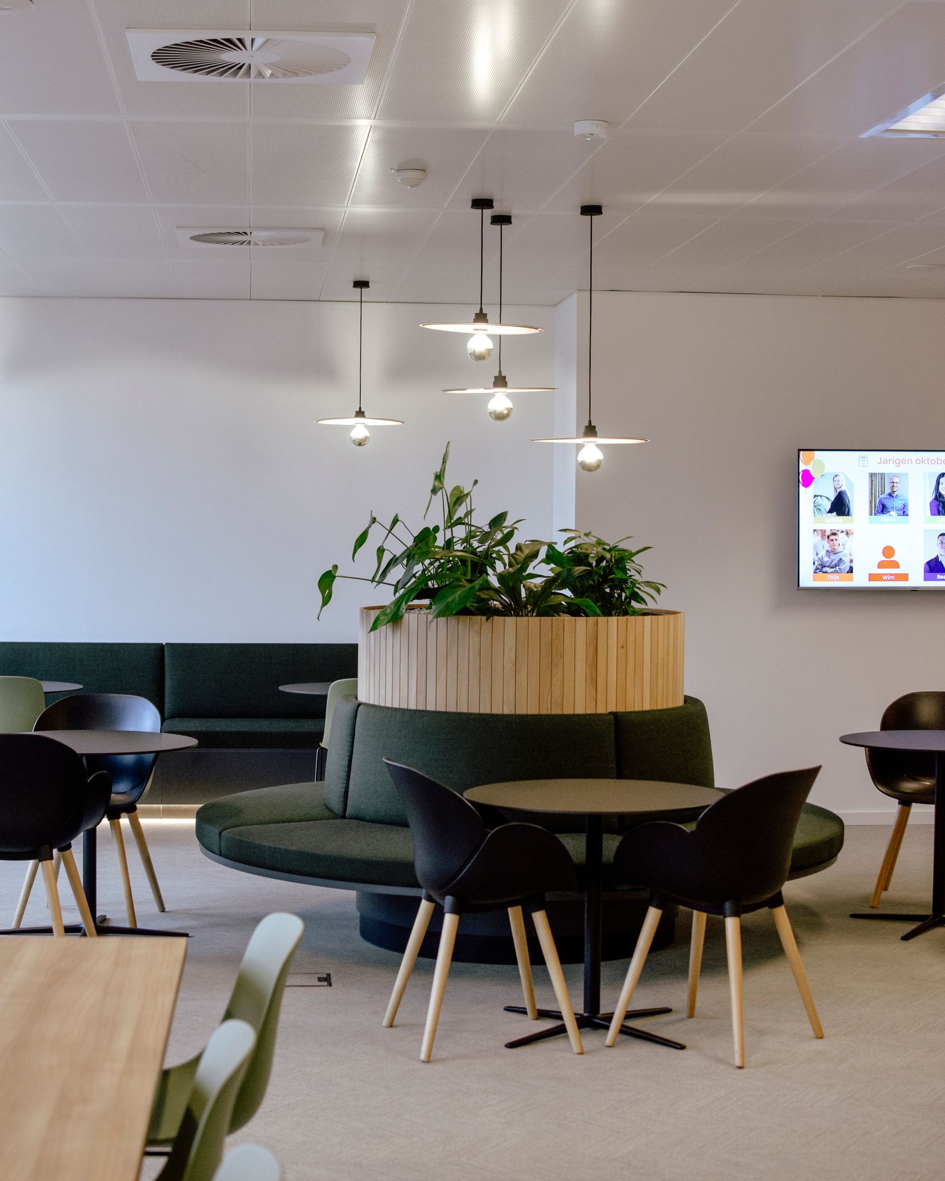 Modern lounge with round tables, dark chairs, hanging lights, and a large planter centerpiece