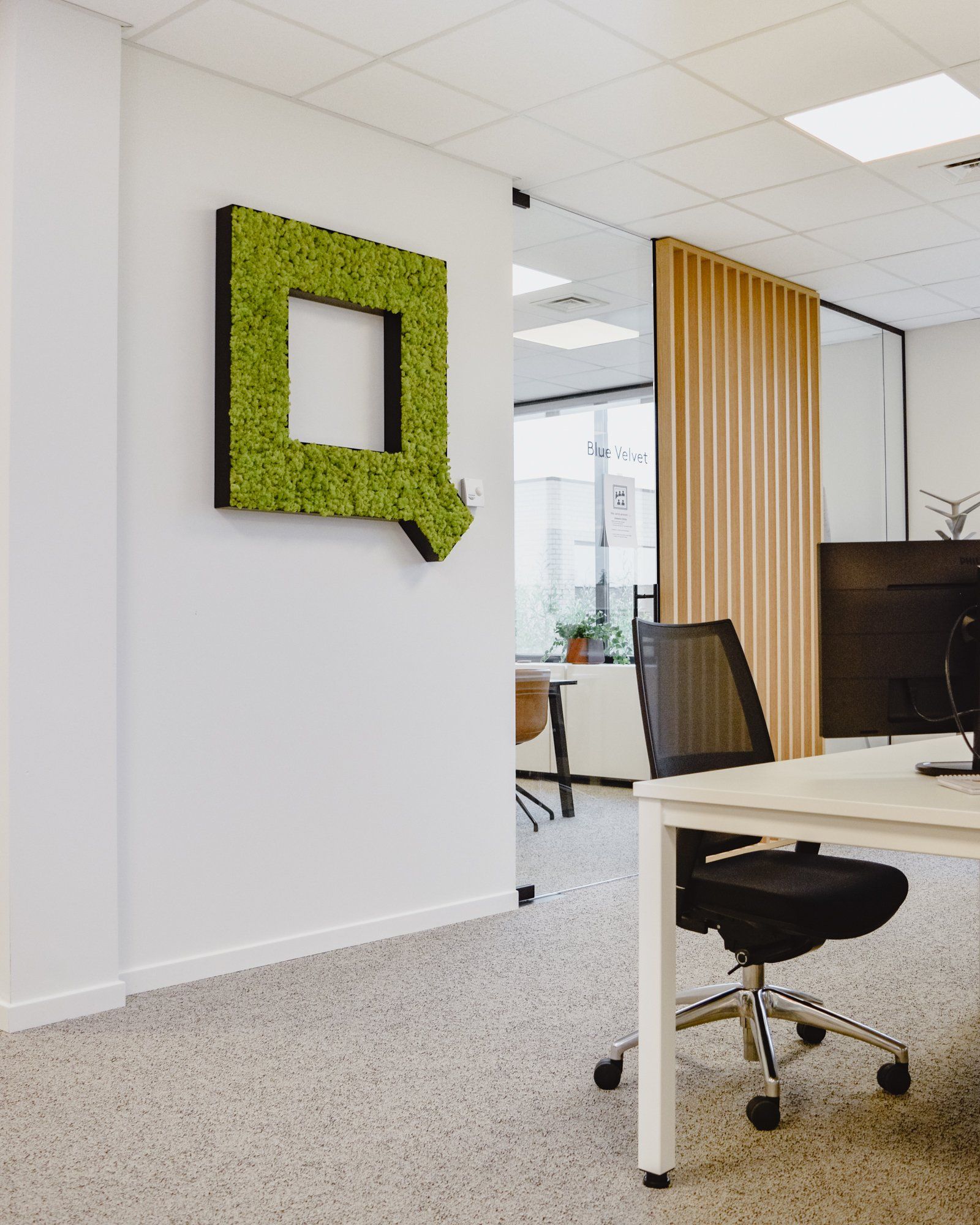 Intérieur de bureau moderne avec bureaux, chaises et logo vert sur un mur blanc.