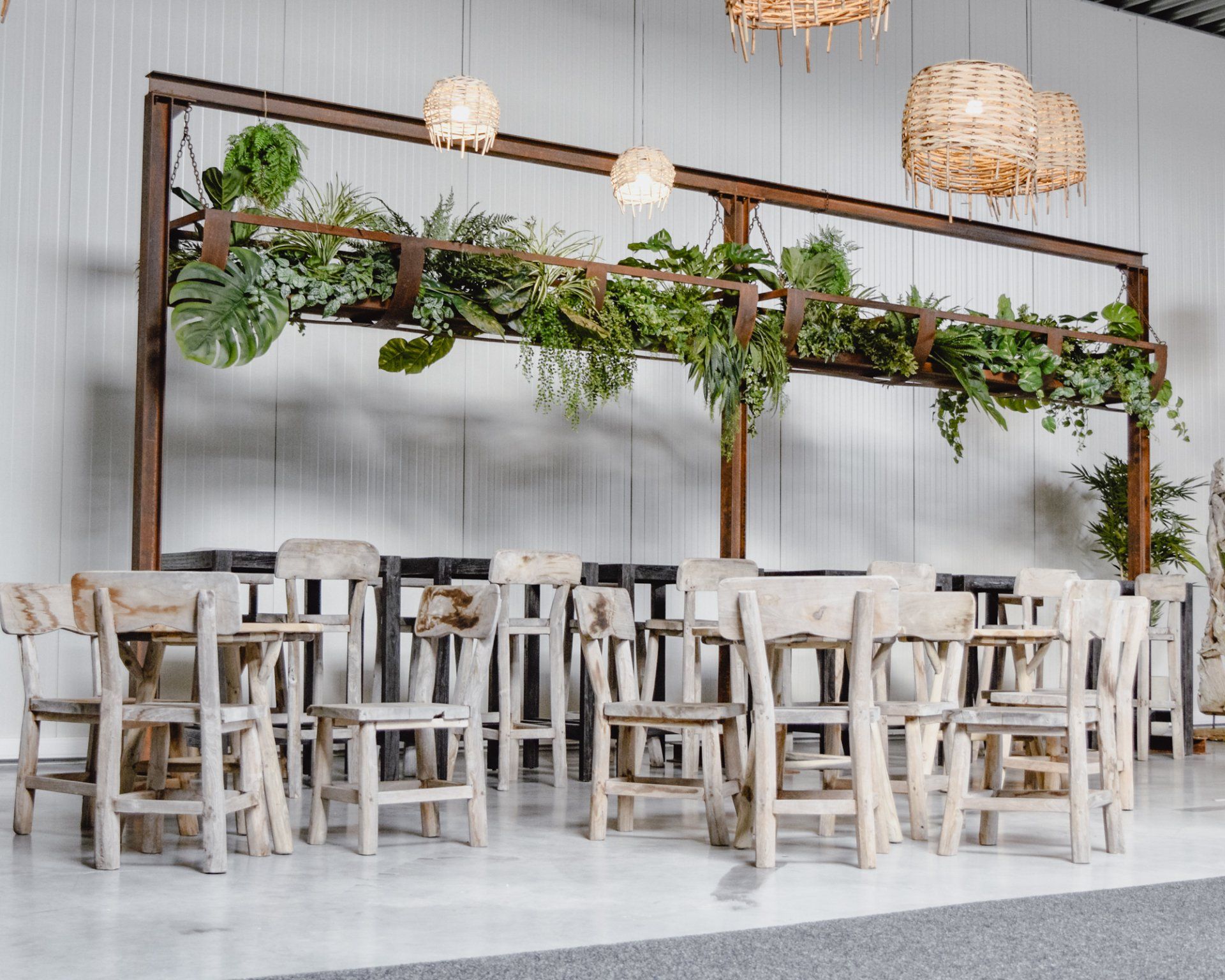 Aménagement rustique d'un événement en intérieur avec tables et chaises en bois, plantes suspendues et guirlandes lumineuses tressées