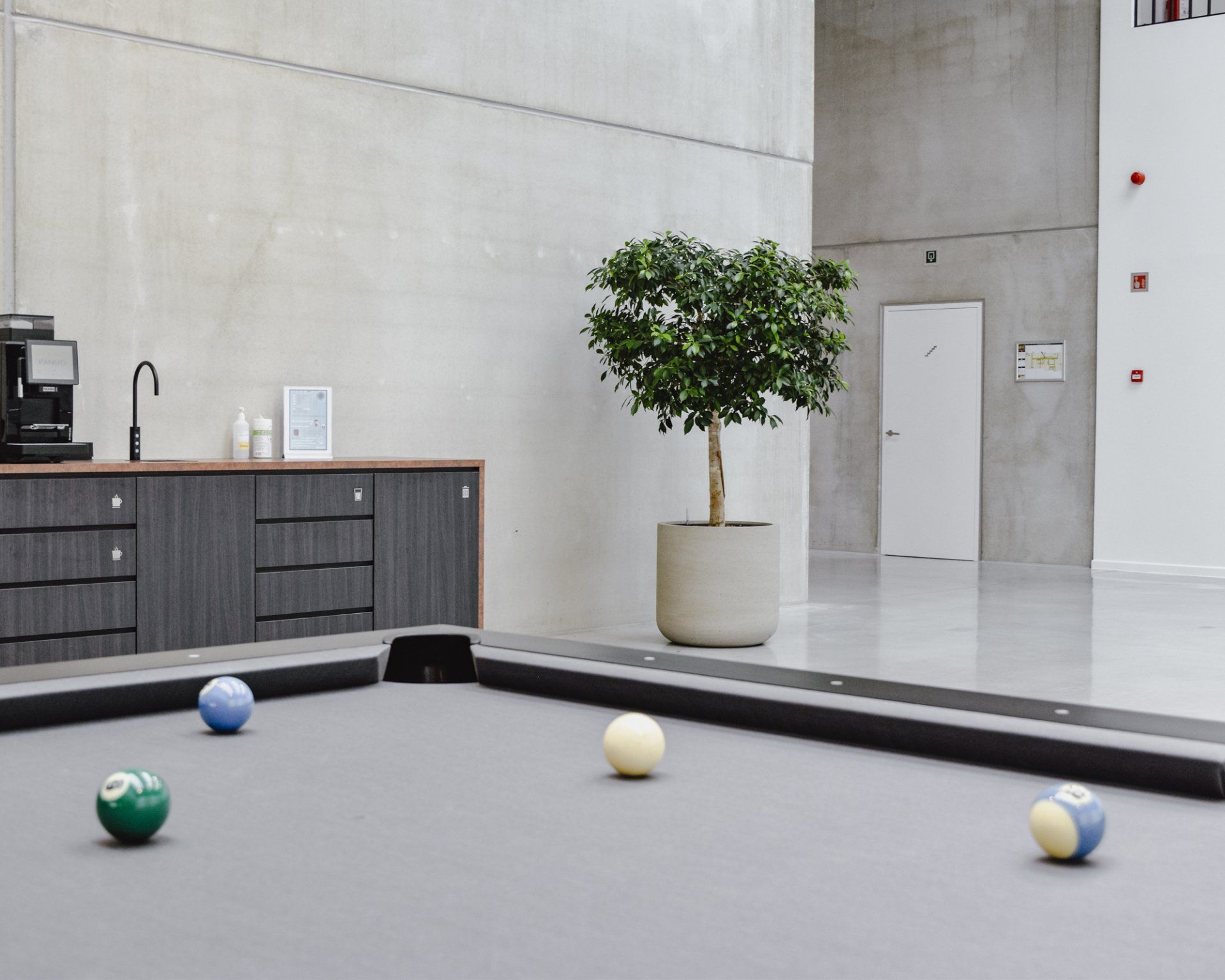 Modern lounge with a pool table and four balls, against a minimalist wall and potted tree