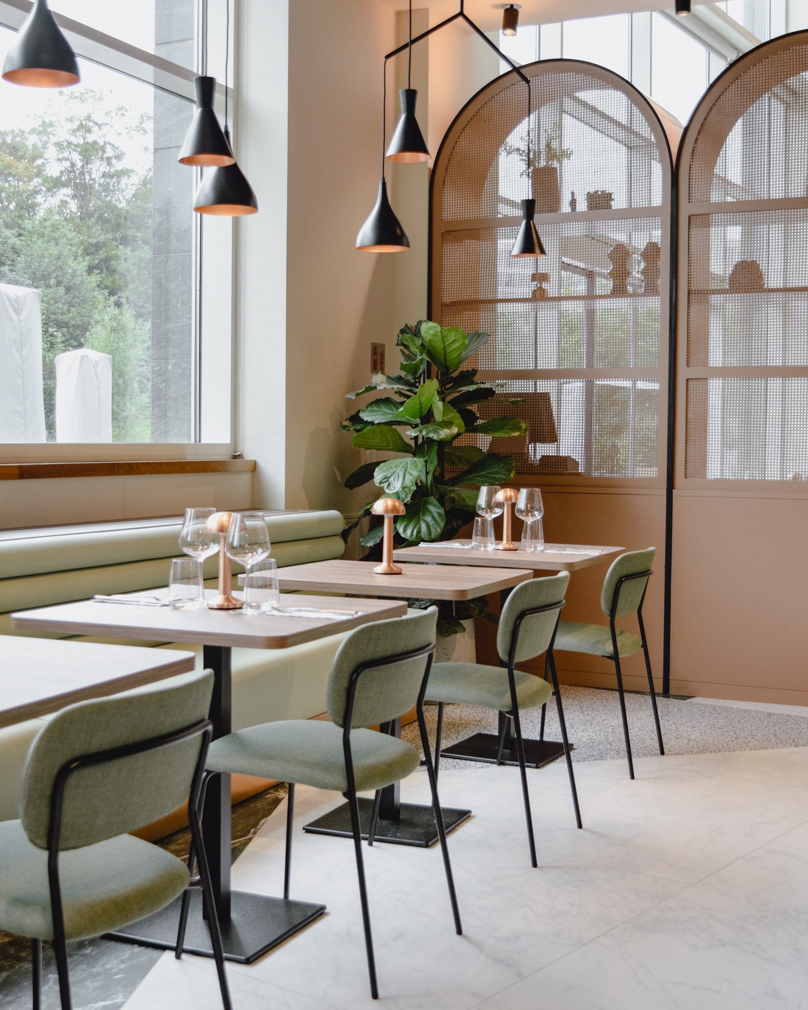 Stylish café interior with green chairs, wooden tables, pendant lights, and large arched rattan screens