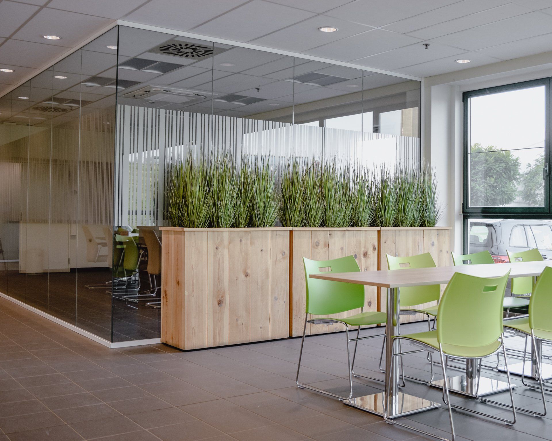 Salon de bureau moderne avec parois vitrées, jardinière en bois et chaises vert citron autour d'une table