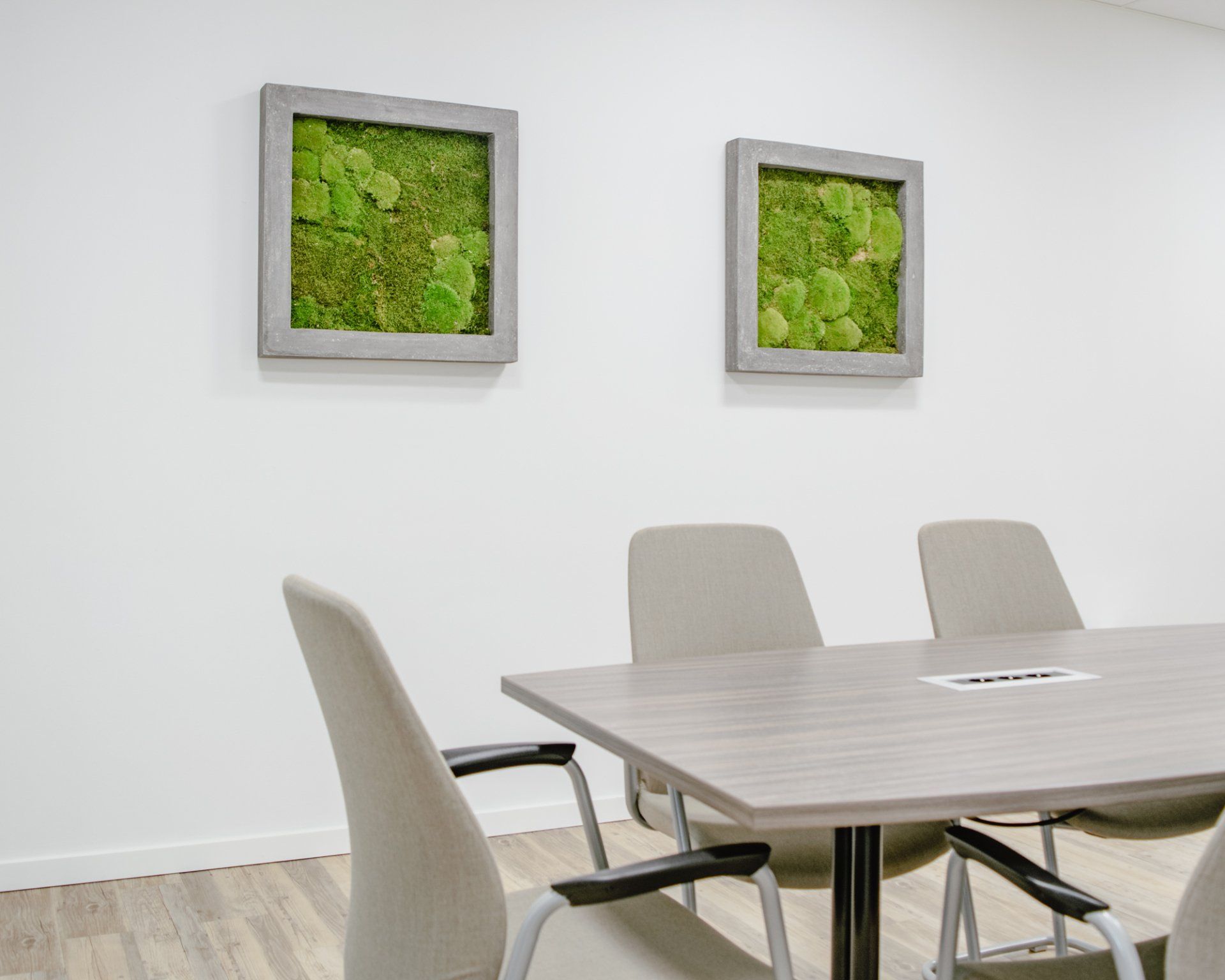Salle de conférence moderne avec une table en bois clair, des chaises beiges et deux tableaux verts encadrés.