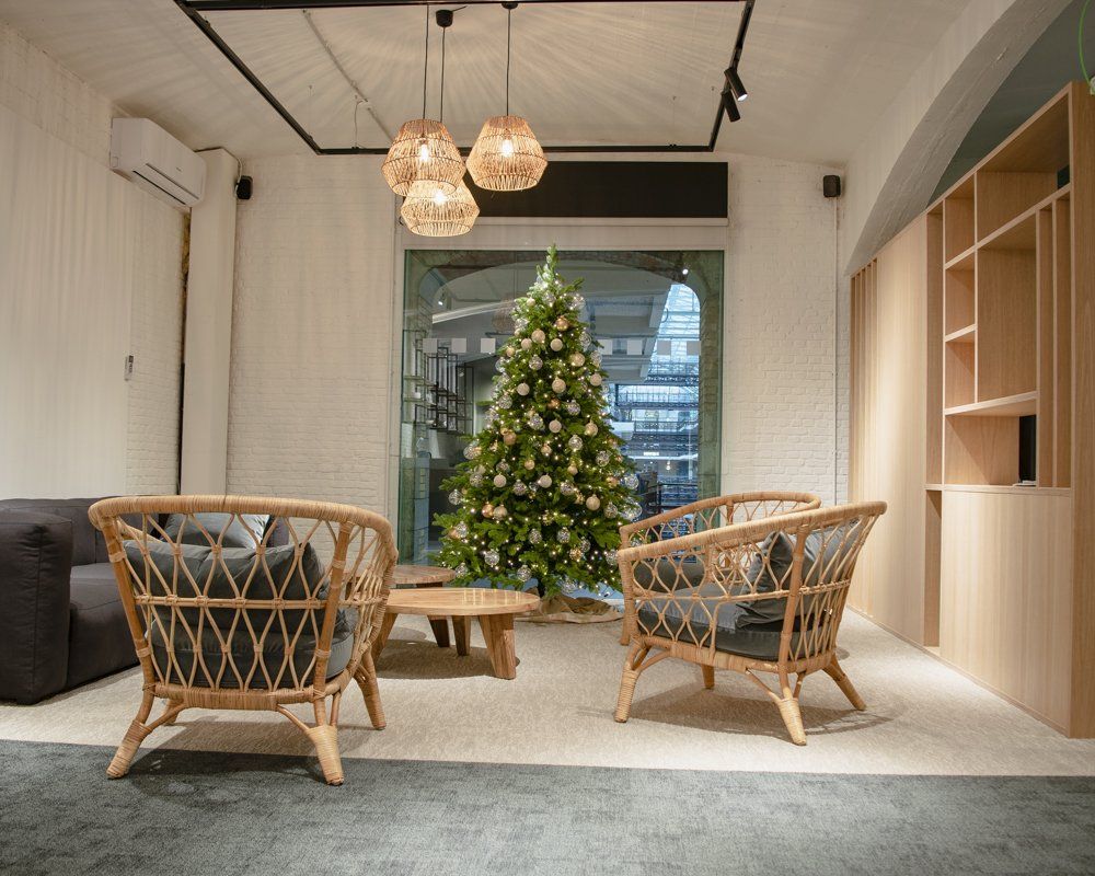 Cozy lounge with wicker chairs, round table, hanging lights, and a decorated Christmas tree near a window.