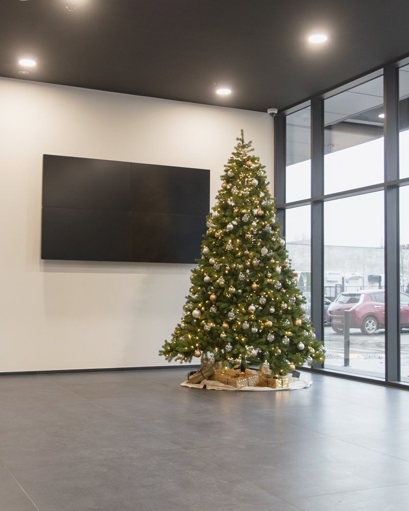 Decorated Christmas tree beside a wall-mounted TV in a modern lobby with large windows