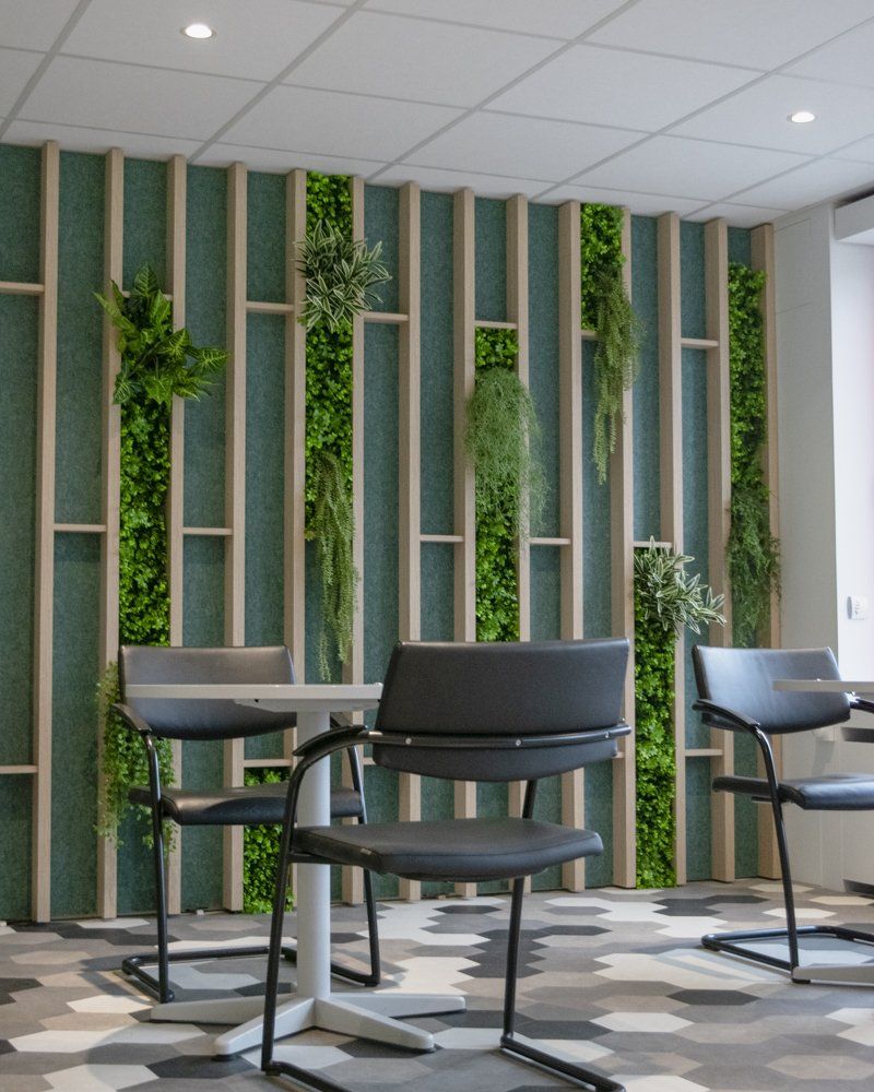 Modern lounge with black chairs and tables against a green vertical plant wall and striped wood panels.