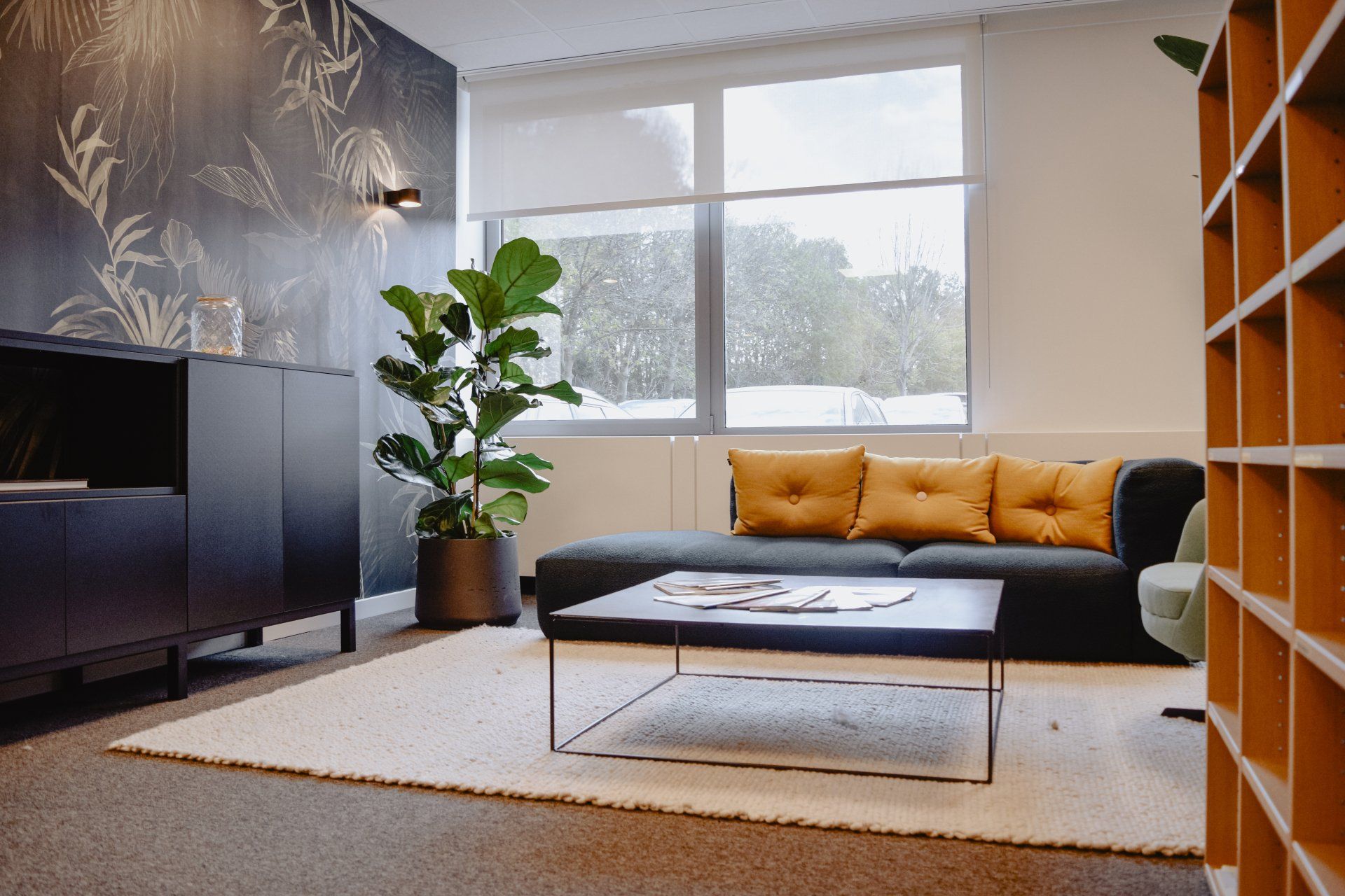 Modern living room with black sofa, mustard pillows, coffee table, plant, and large window with snowy view