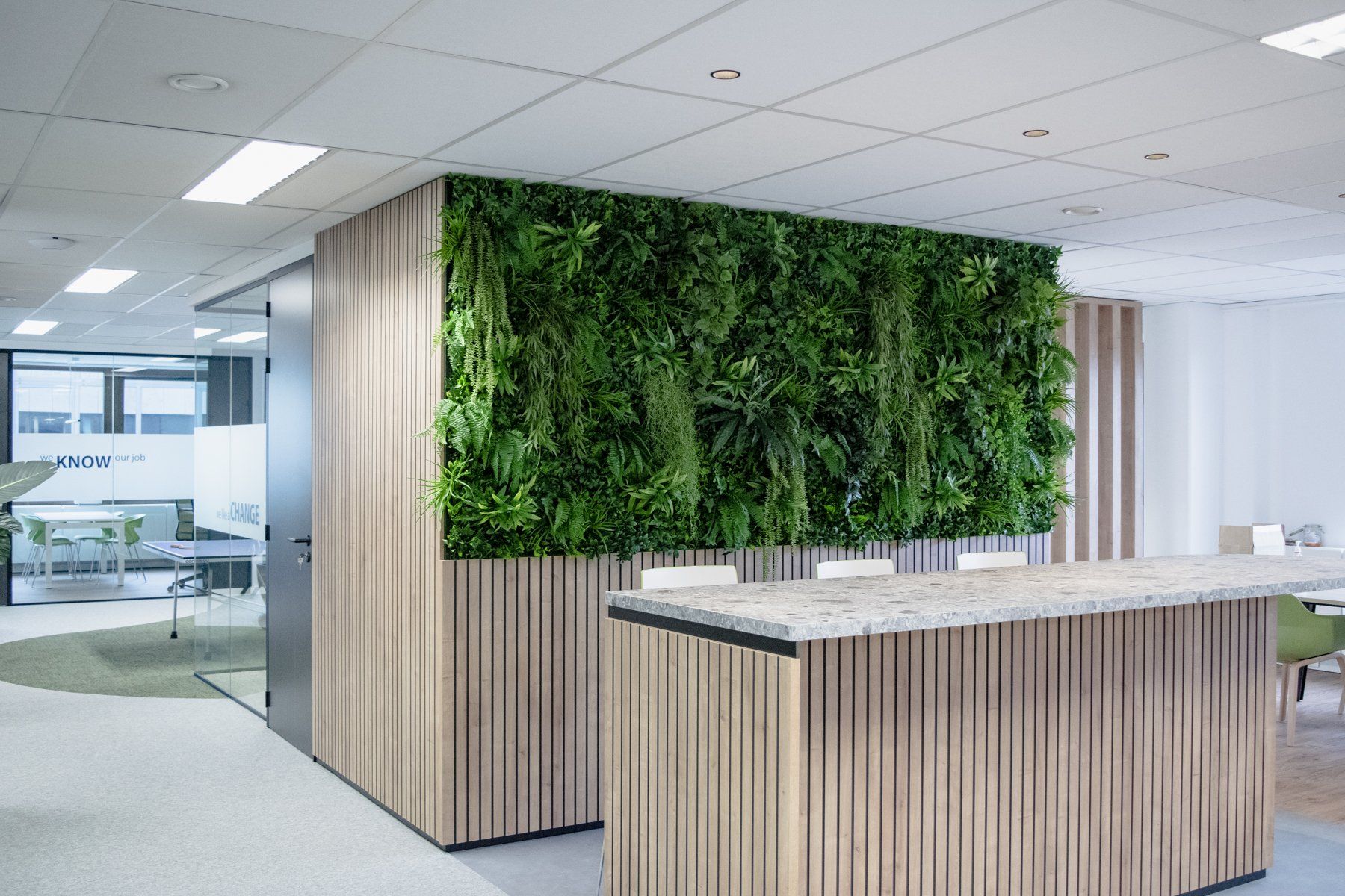 Hall d'entrée moderne avec comptoir d'accueil en bois et mur végétal sous un éclairage lumineux au plafond.