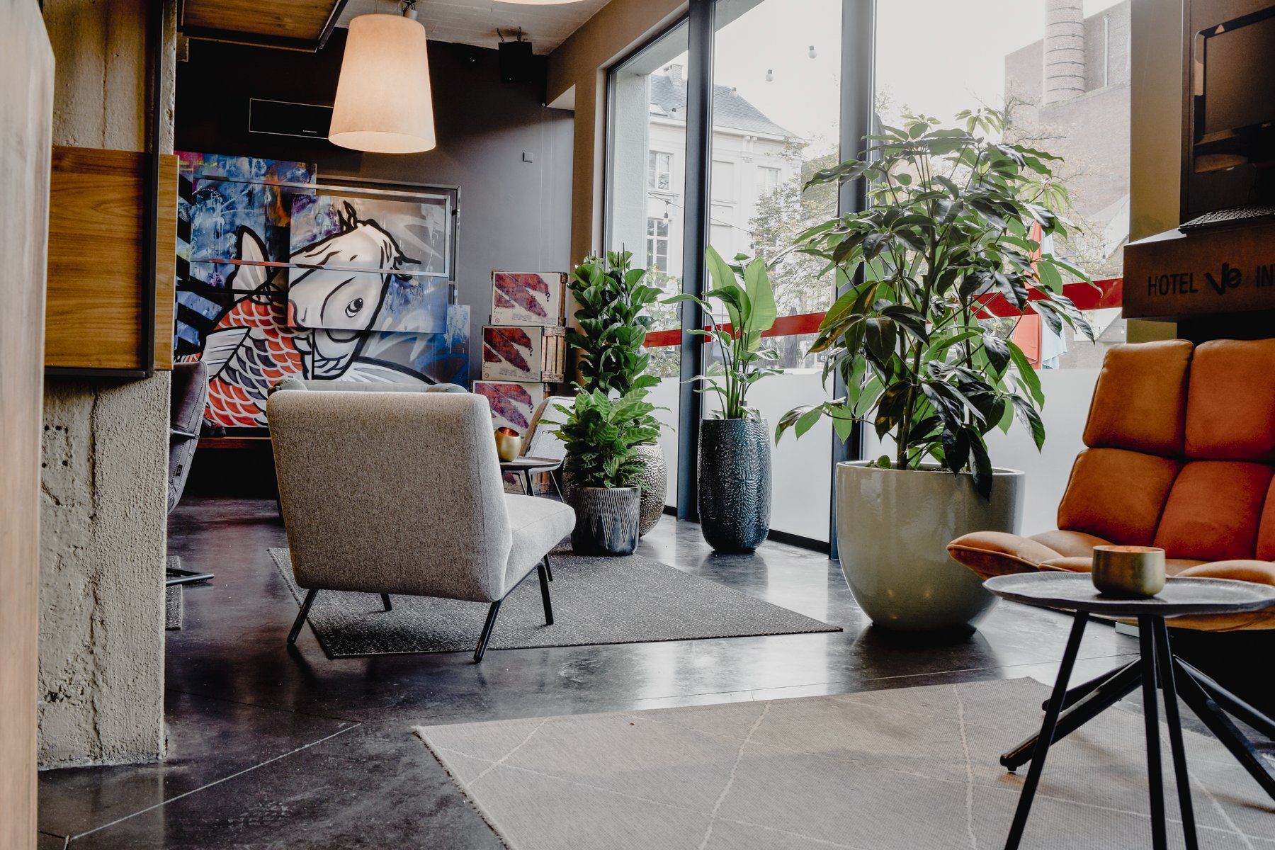 Modern lounge with chairs, plants, large windows, and colorful wall art in a cozy interior.