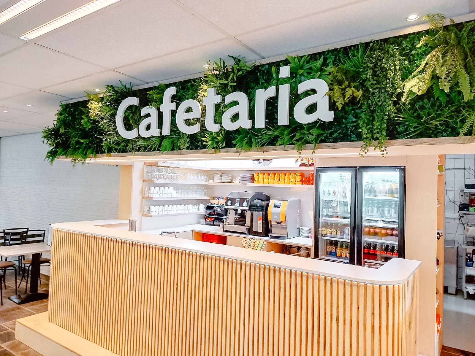 Comptoir de cafétéria avec lattes de bois, machines à café, réfrigérateurs et décoration végétale