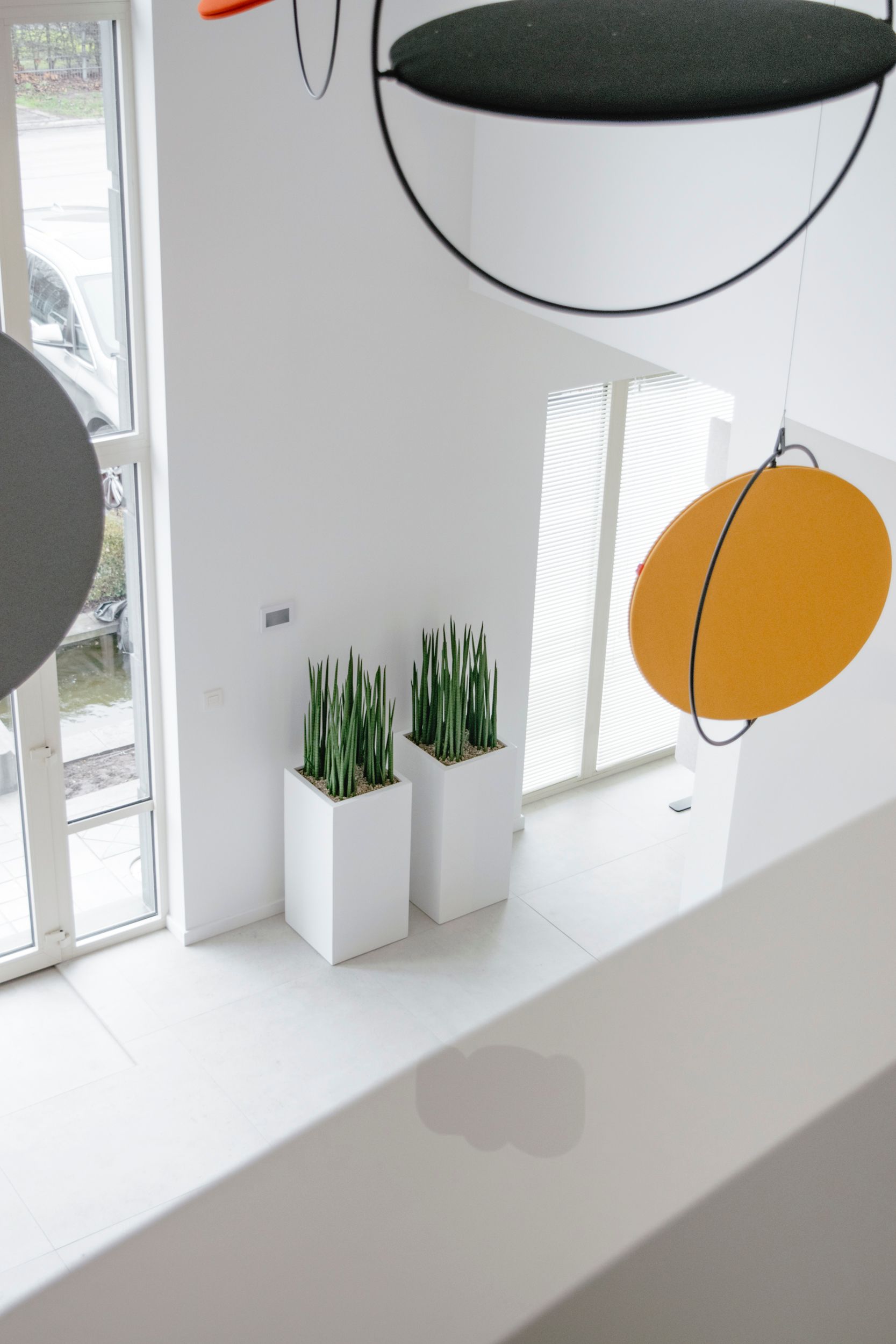Des plantes en pot sur un rebord de fenêtre blanc, à côté d'une décoration circulaire suspendue et d'un disque jaune près d'une fenêtre lumineuse.