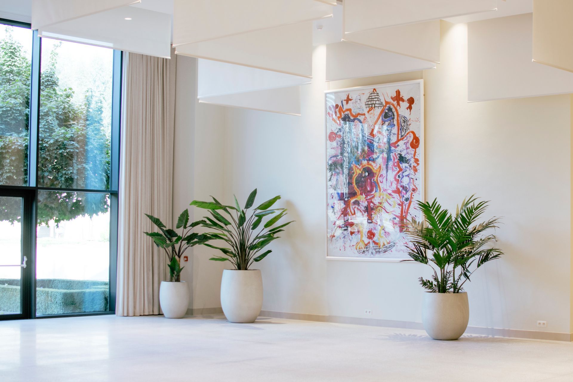 Hall d'entrée minimaliste et lumineux avec plantes en pot, œuvres d'art abstraites aux murs et grandes fenêtres laissant entrer la lumière naturelle