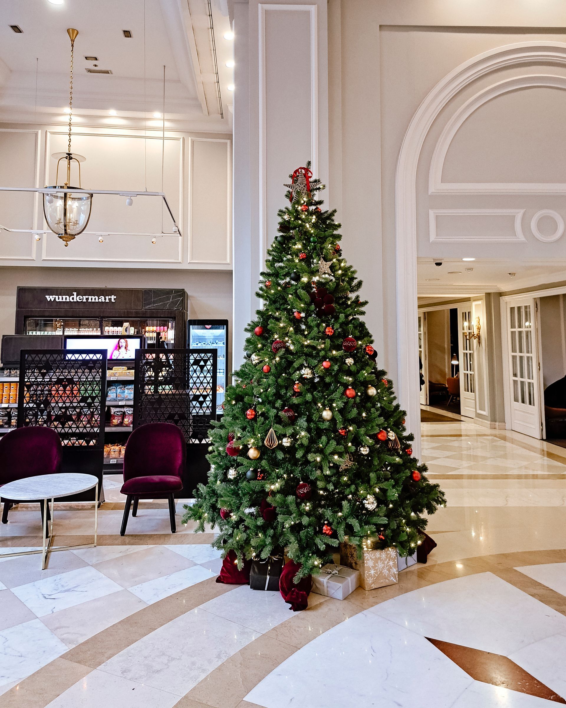 Decorated Christmas tree in a luxury hotel lobby with marble floors and a café in the background