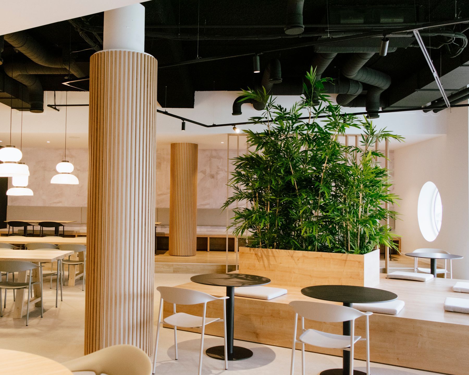 Salon de bureau moderne avec colonnes en bois, tables rondes, chaises et grandes plantes d'intérieur dans un espace ouvert et lumineux