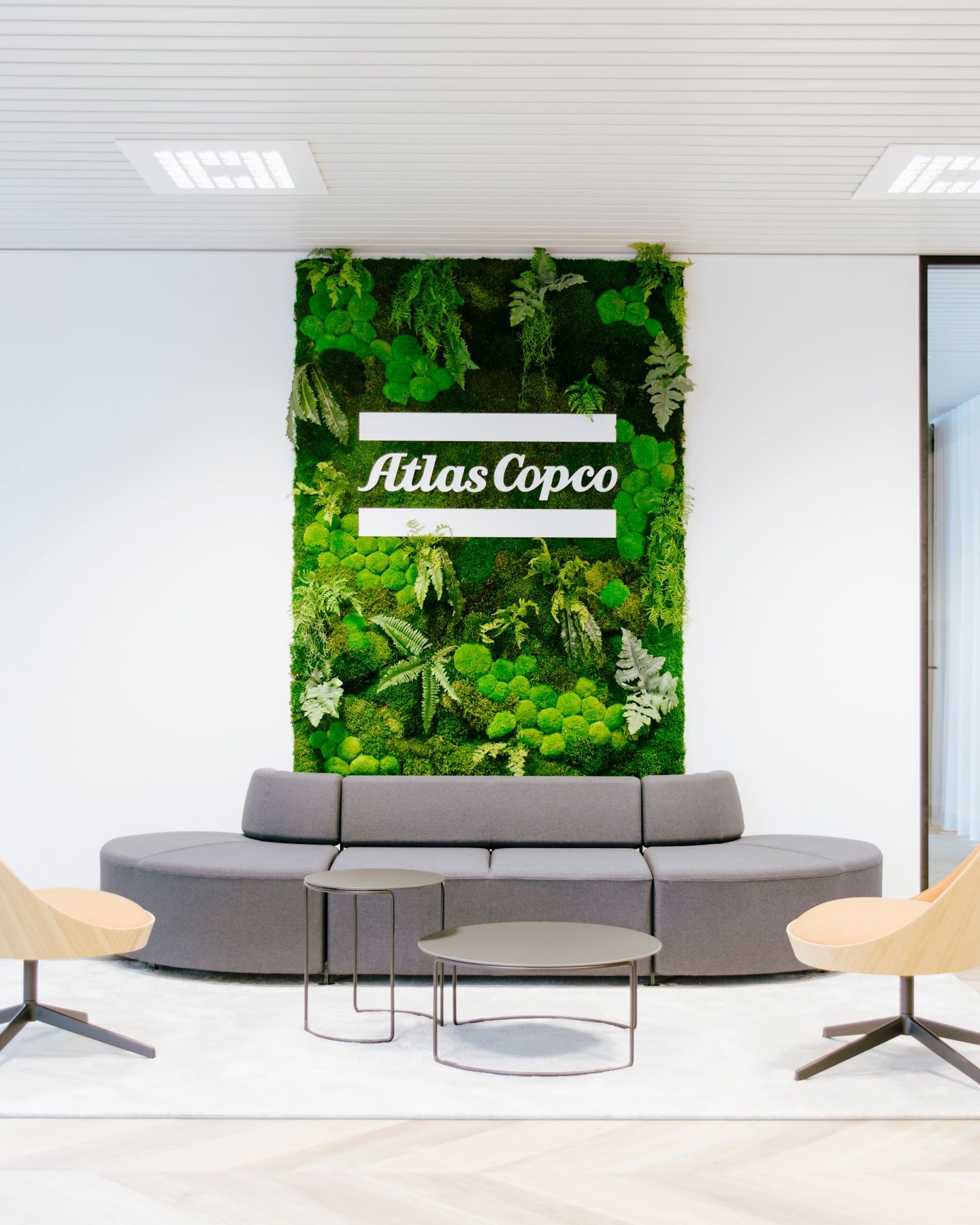 Modern lounge with gray sofa, coffee tables, and a green plant wall featuring the “Hias Copco” sign