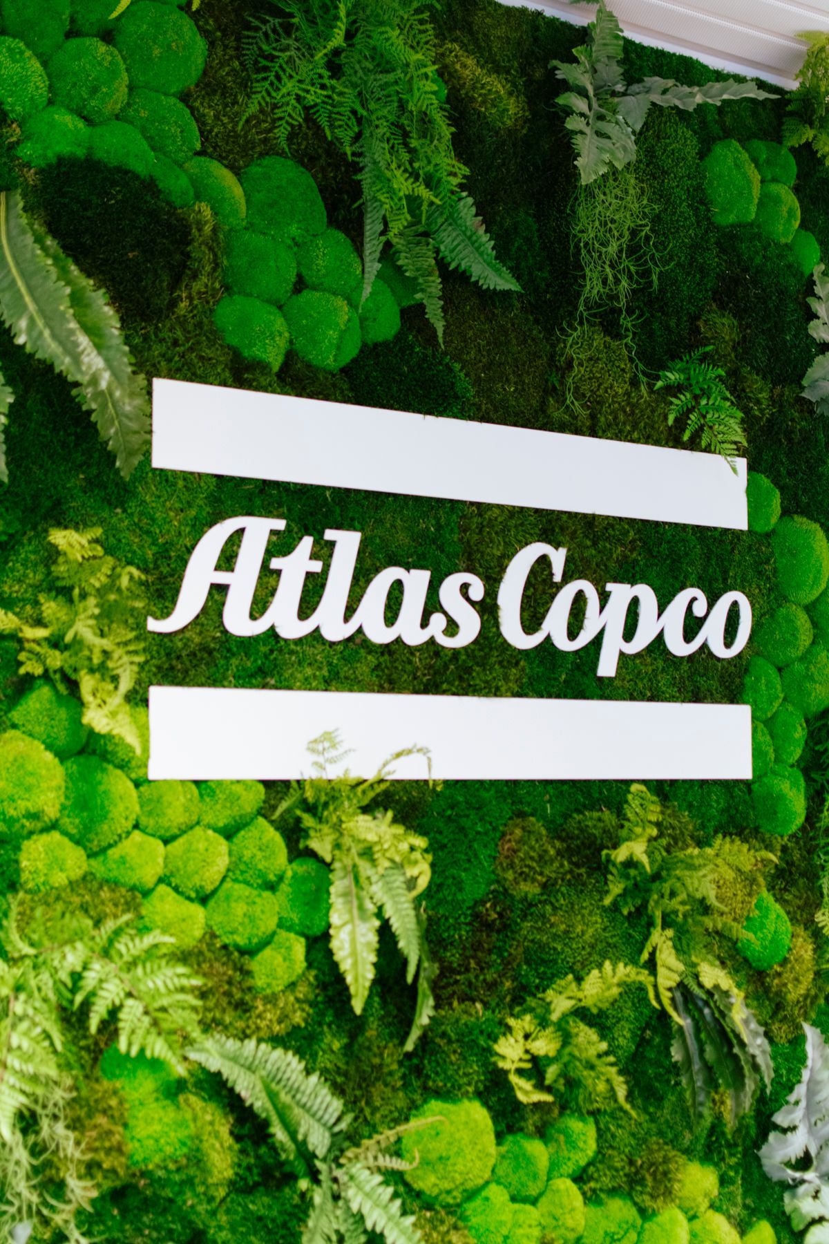 Logo Atlas Copco sur un mur recouvert de mousse verte avec des panneaux horizontaux blancs