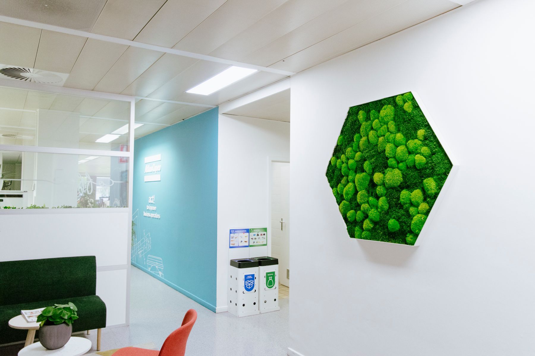 Couloir de bureau moderne avec un panneau mural hexagonal vert et une porte en verre bleu près d'un coin détente