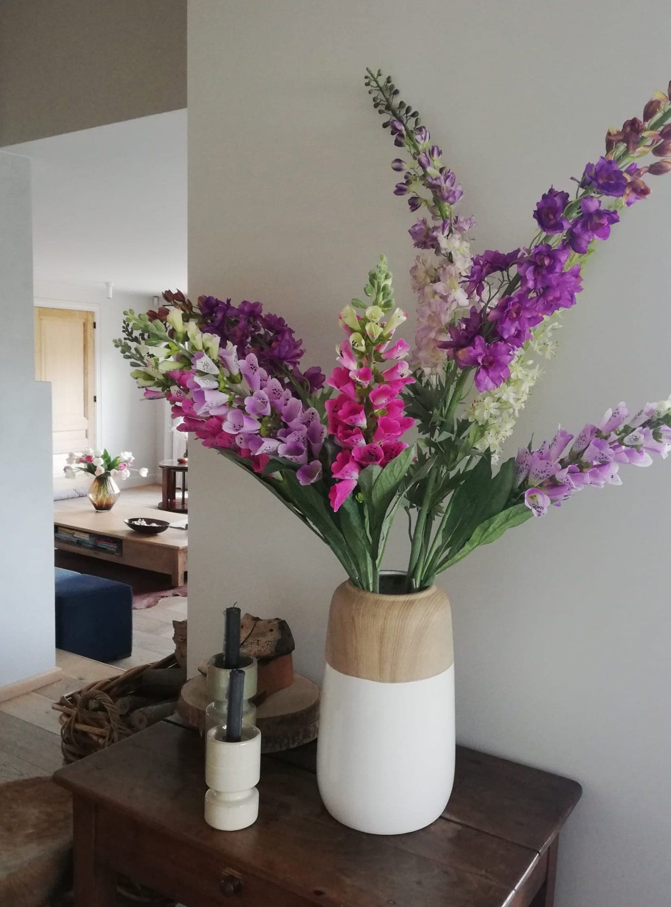 White vase with purple and pink flowers on a wooden table in a home interior