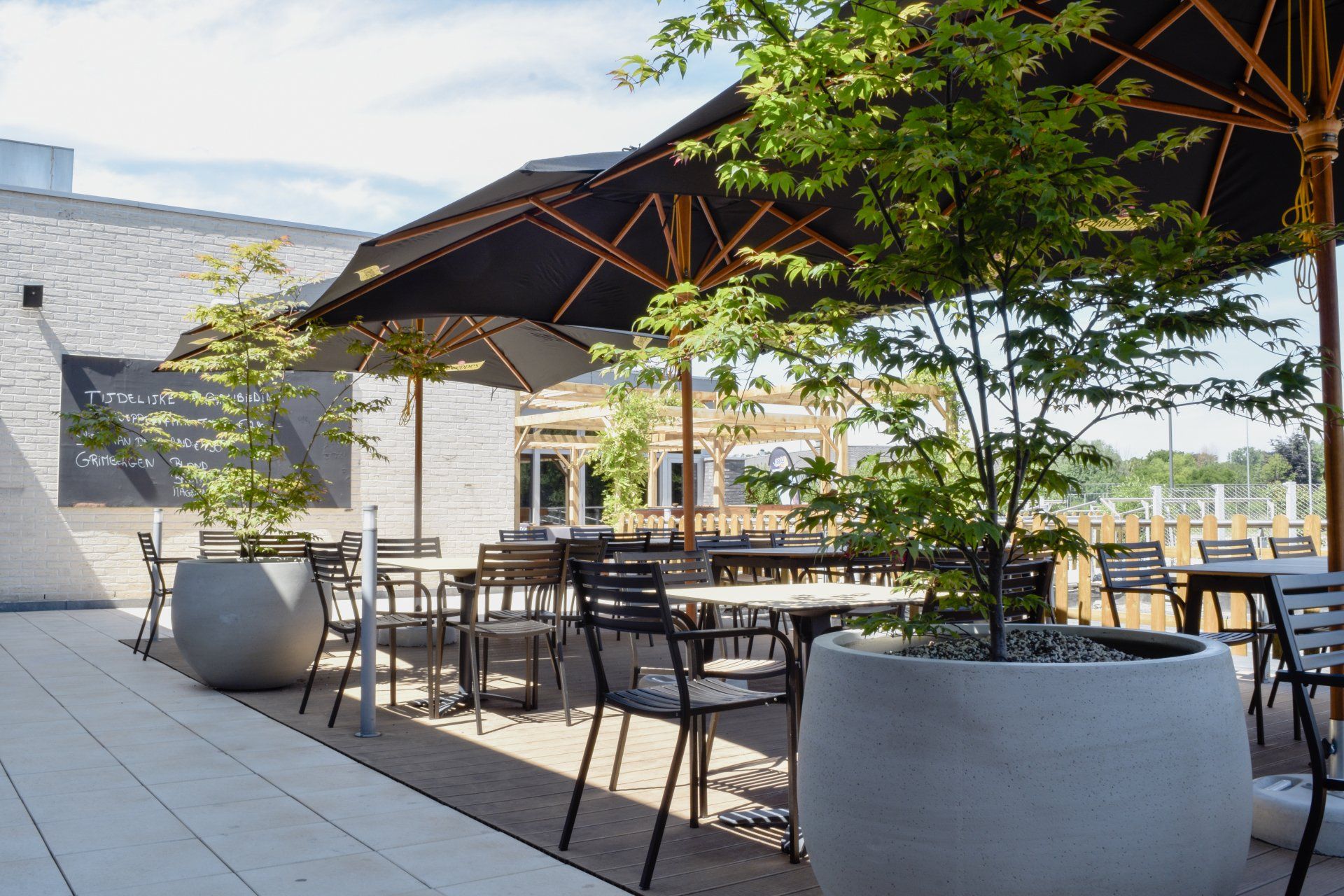 Outdoor café patio with black tables, umbrellas, and potted plants on a sunny terrace