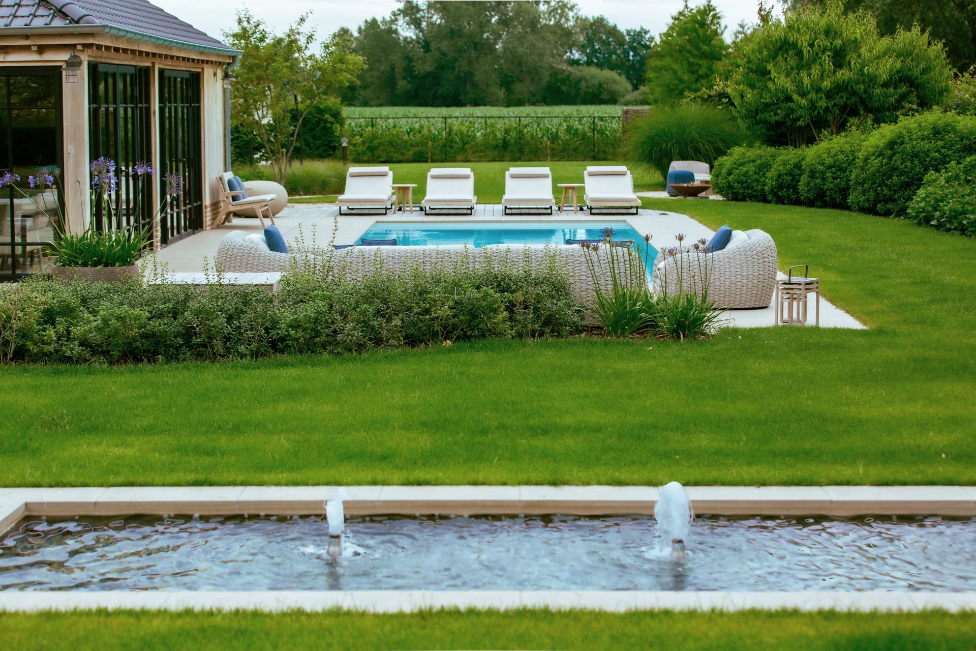 Backyard pool with white lounge chairs, green lawn, and a narrow reflecting pool in the foreground