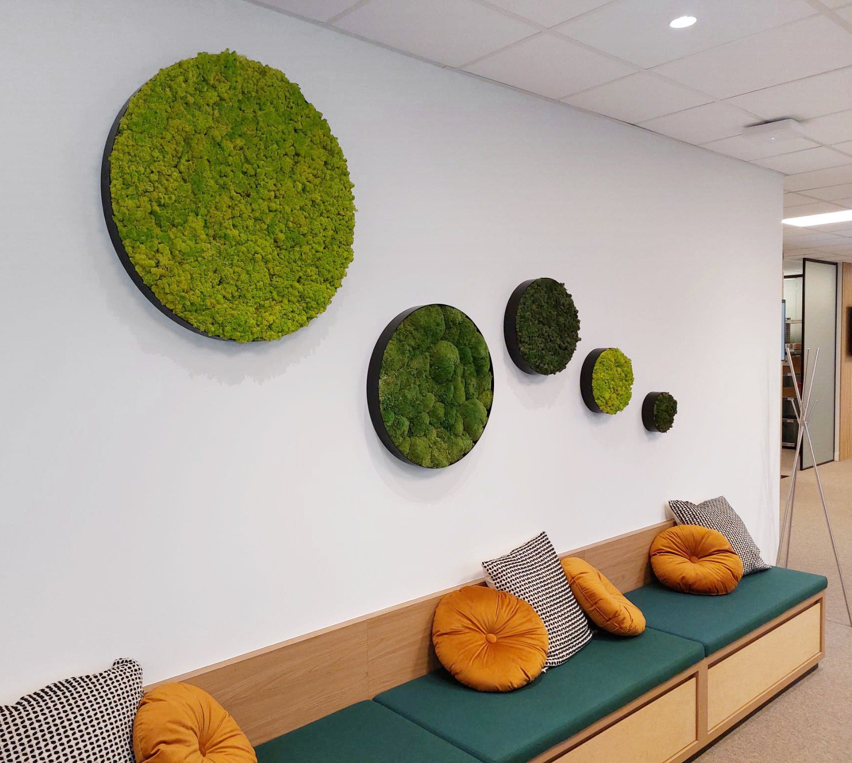 Modern lounge with moss wall art, teal bench seating, and orange cushions in a bright hallway.