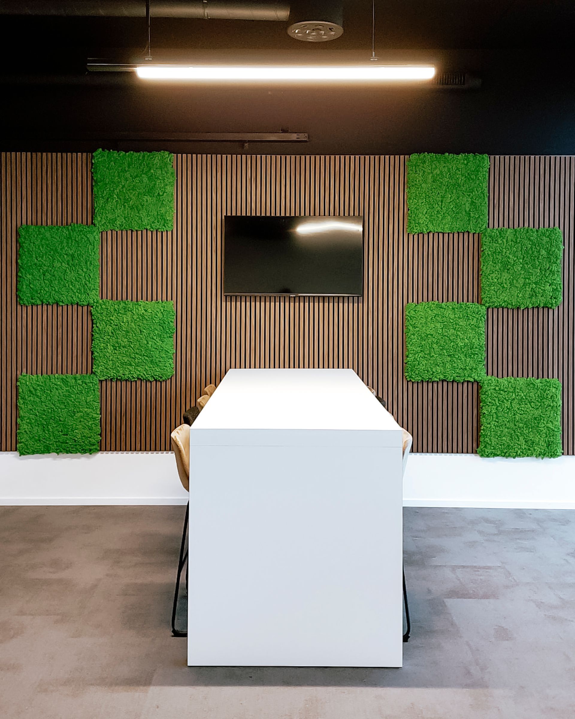 Hall d'entrée moderne avec un podium blanc, une télévision murale et des panneaux végétaux verts sur un mur en bois rayé.