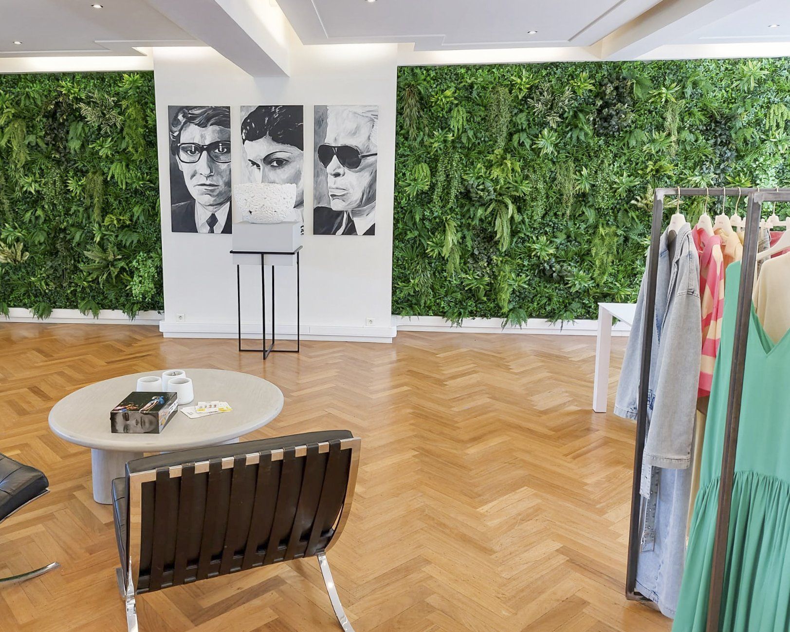 Showroom moderne avec mur vert, parquet à chevrons, œuvres d'art en noir et blanc et portant à vêtements aux tons pastel.