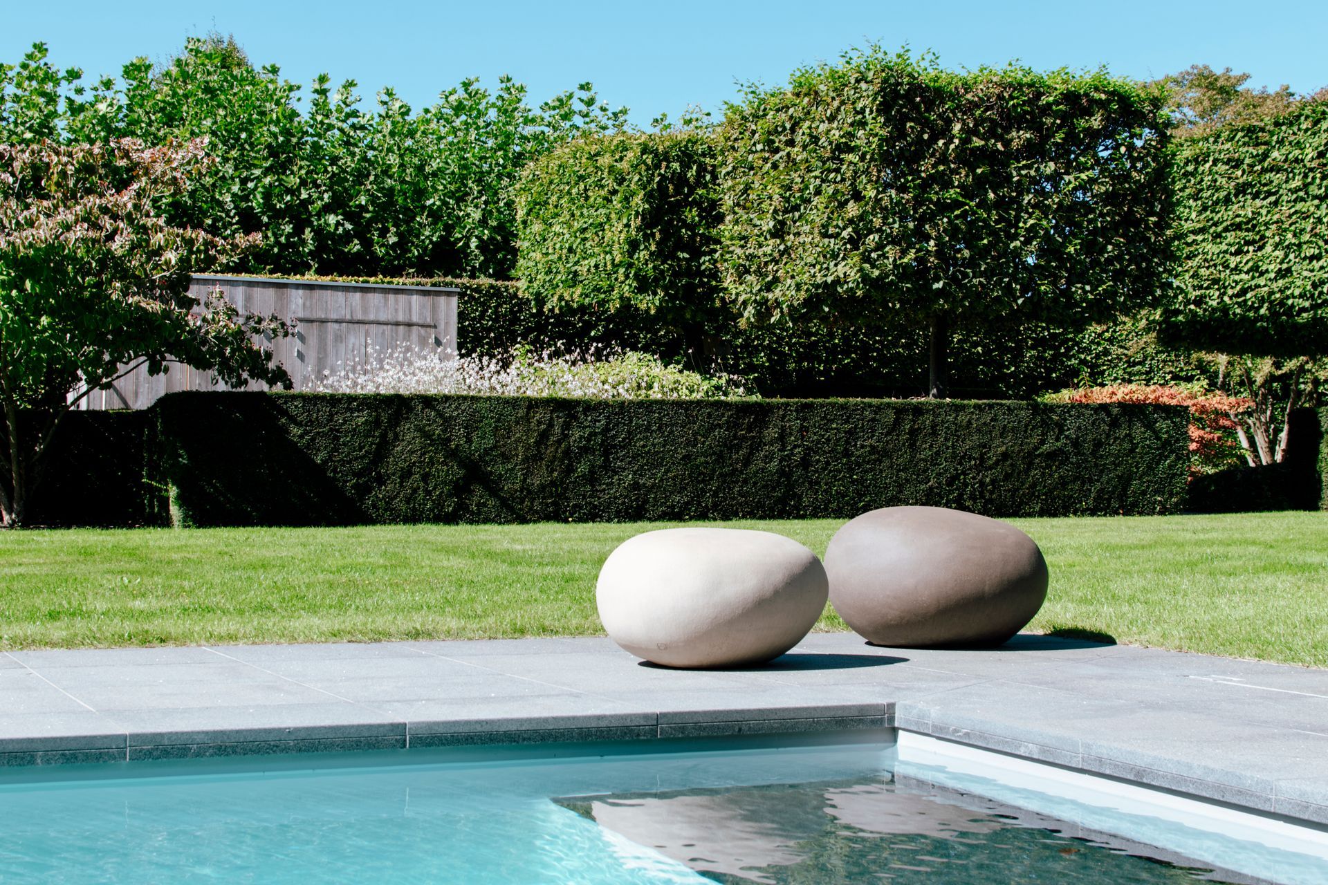 Modern backyard pool with two round stone benches beside a green lawn and hedges