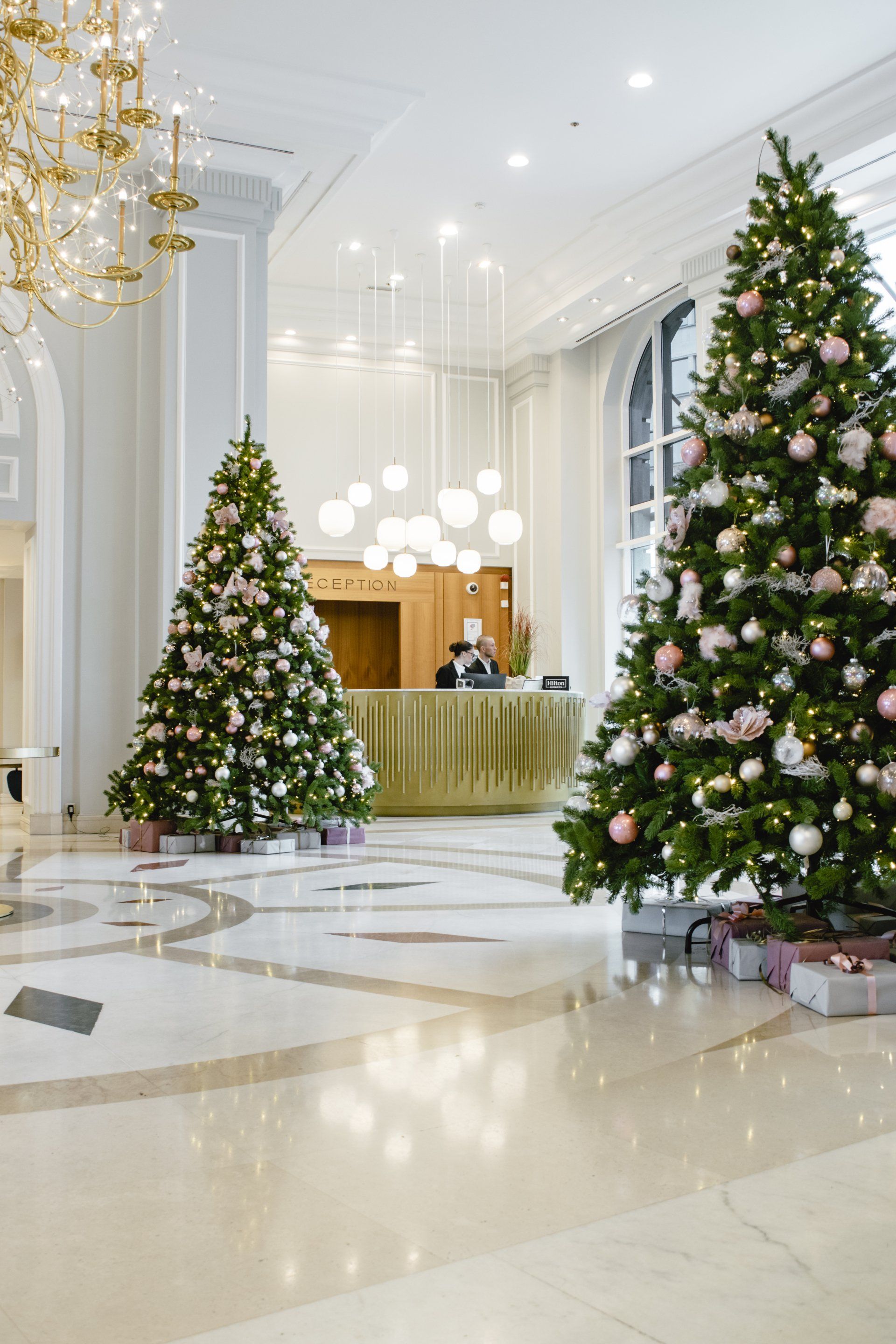 Elegant hotel lobby with two decorated Christmas trees and a reception desk, bright marble floor