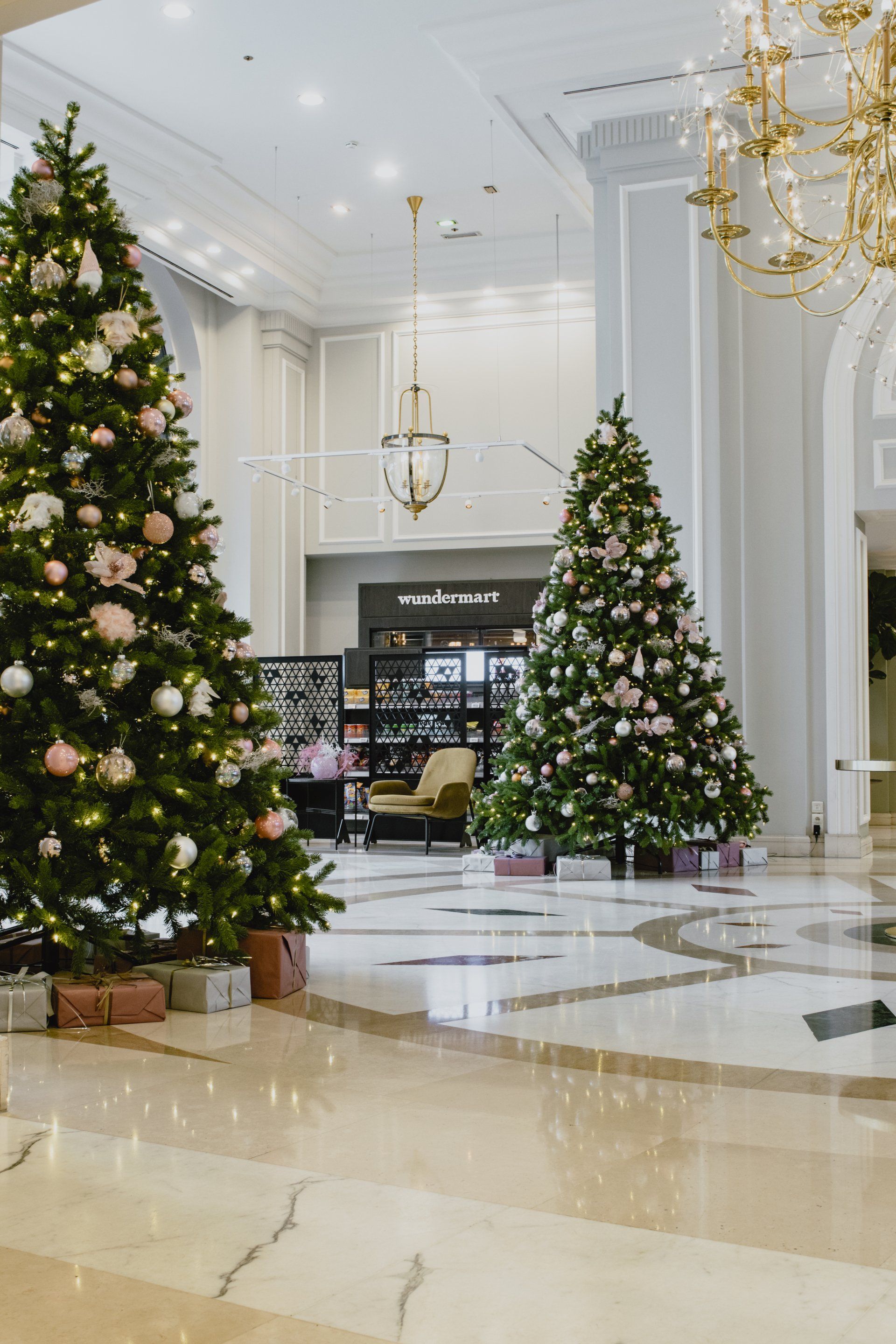 Elegant hotel lobby with two decorated Christmas trees, chandeliers, and marble floors