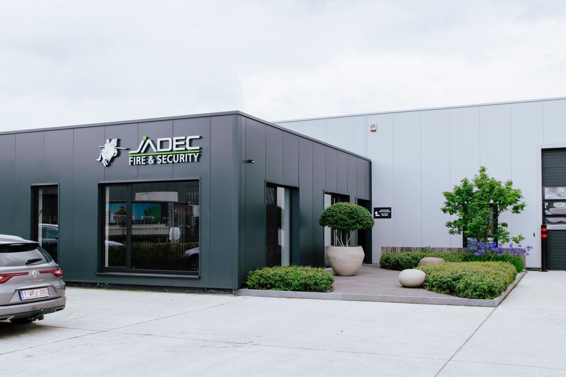 Modern office building with dark gray entrance, white exterior, and landscaped entryway