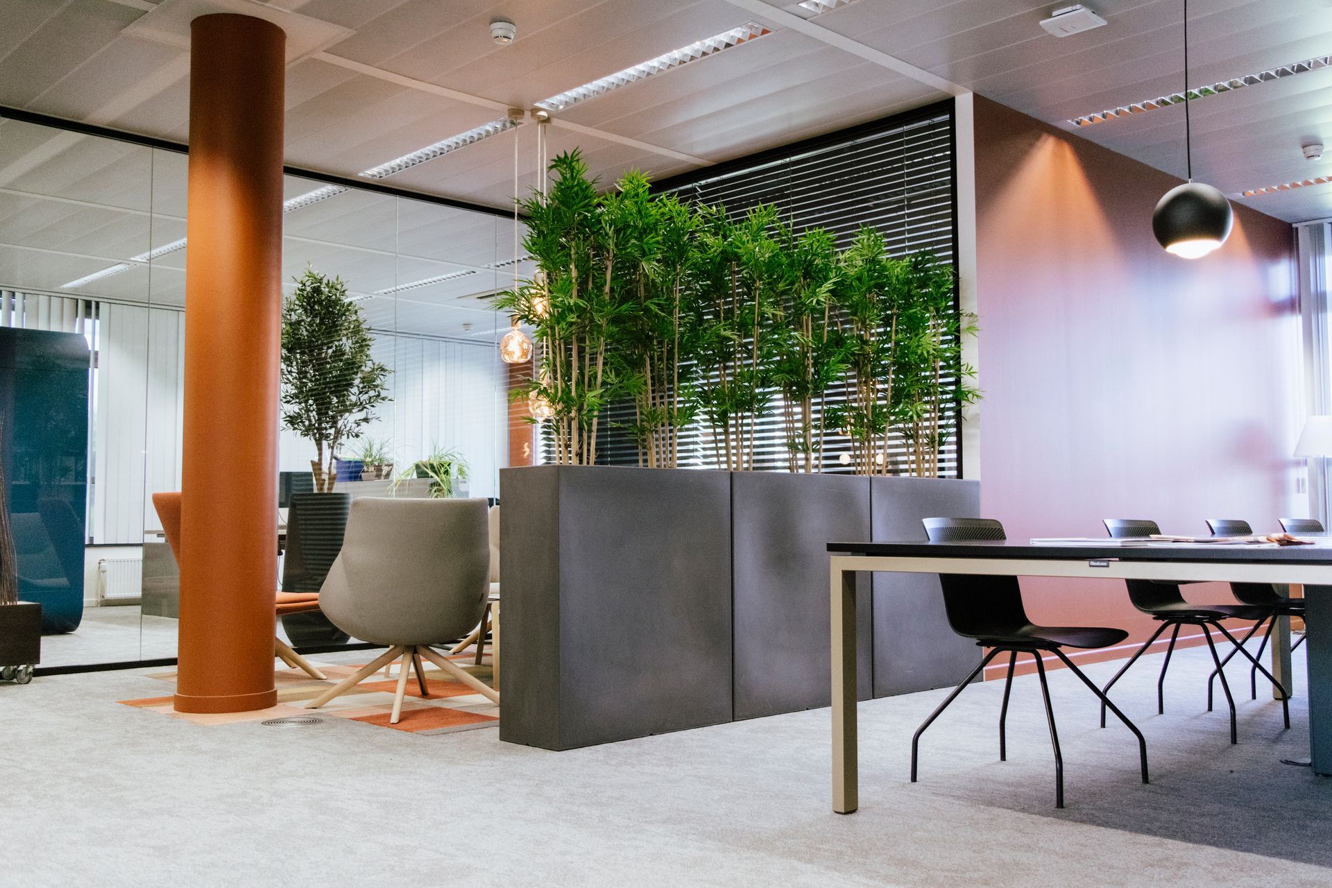 Salon de bureau moderne avec pilier en bois, sièges gris, bureau et plantes d'intérieur derrière une cloison
