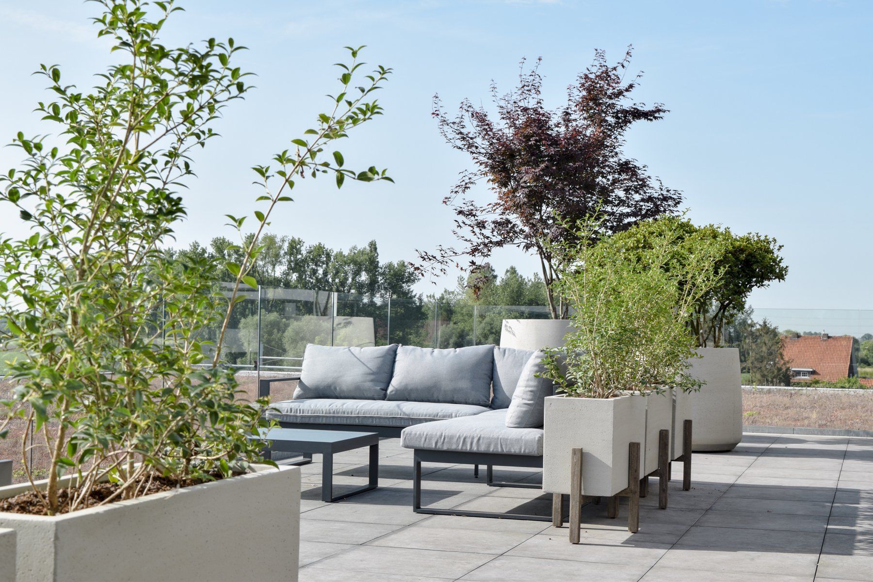 Modern rooftop patio with gray sectional sofa, planters, and city views