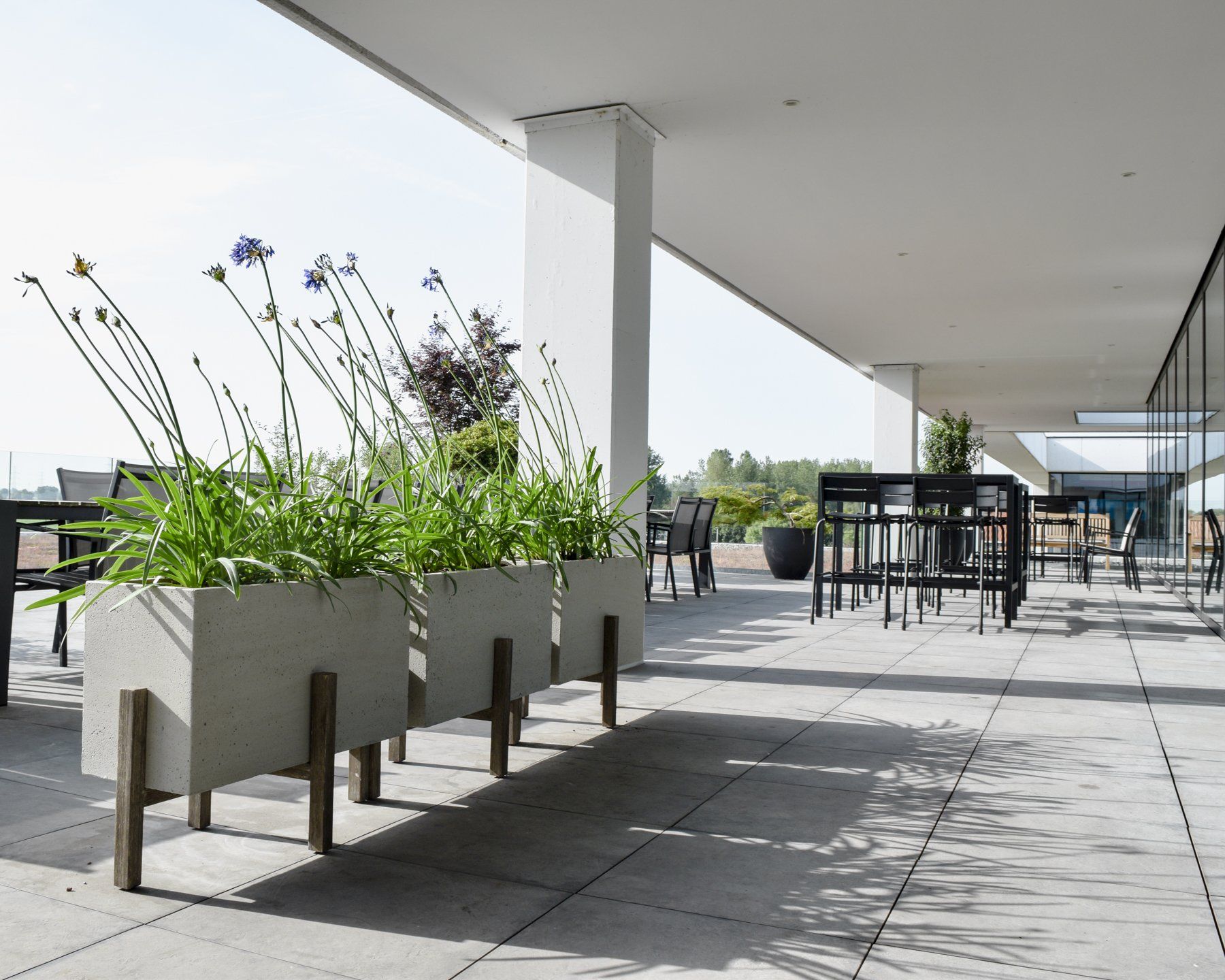 Modern rooftop terrace with concrete planters, black tables, and chairs under a covered walkway