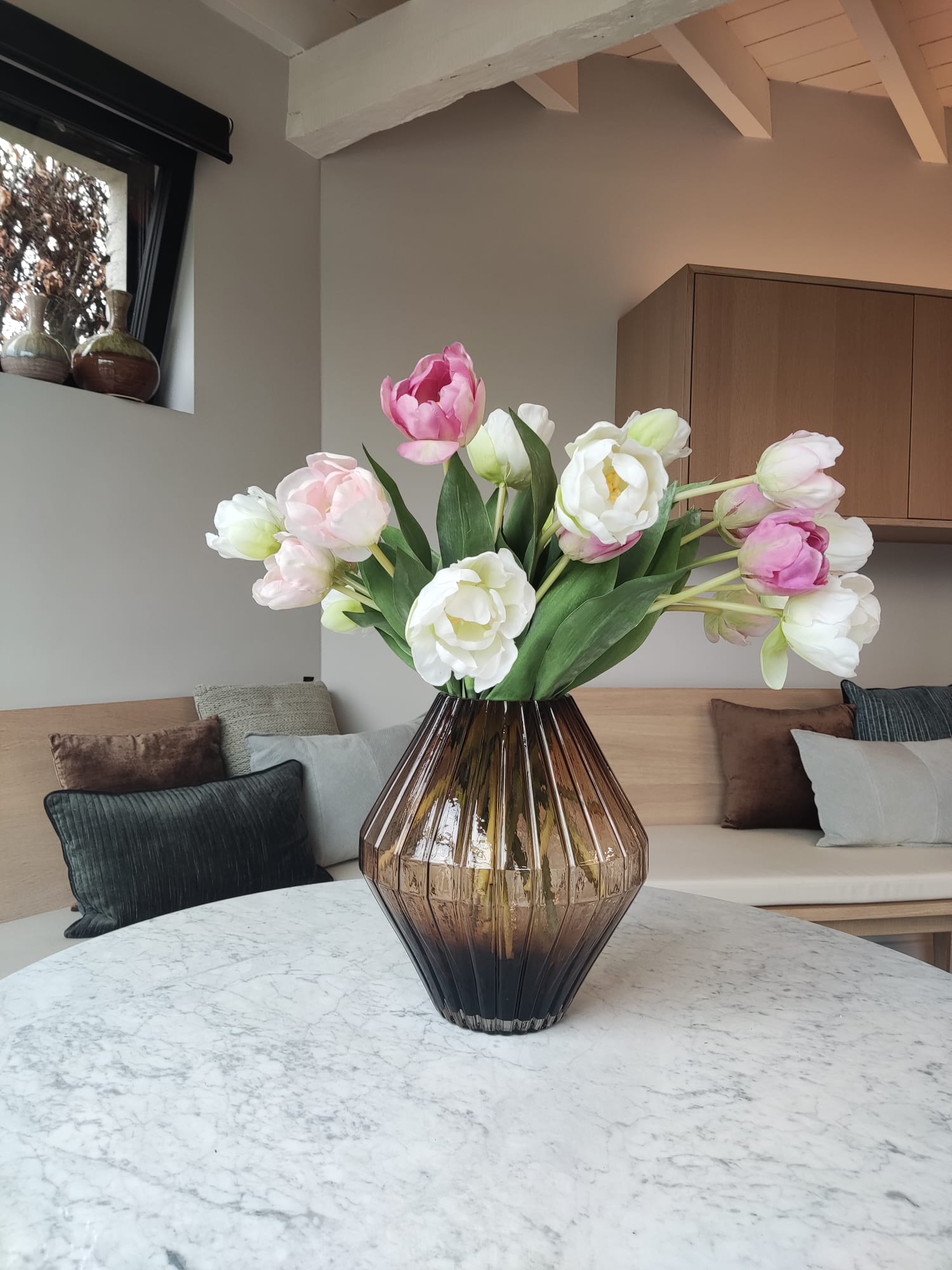 Pink and white tulips in a brown glass vase on a coffee table in a modern living room
