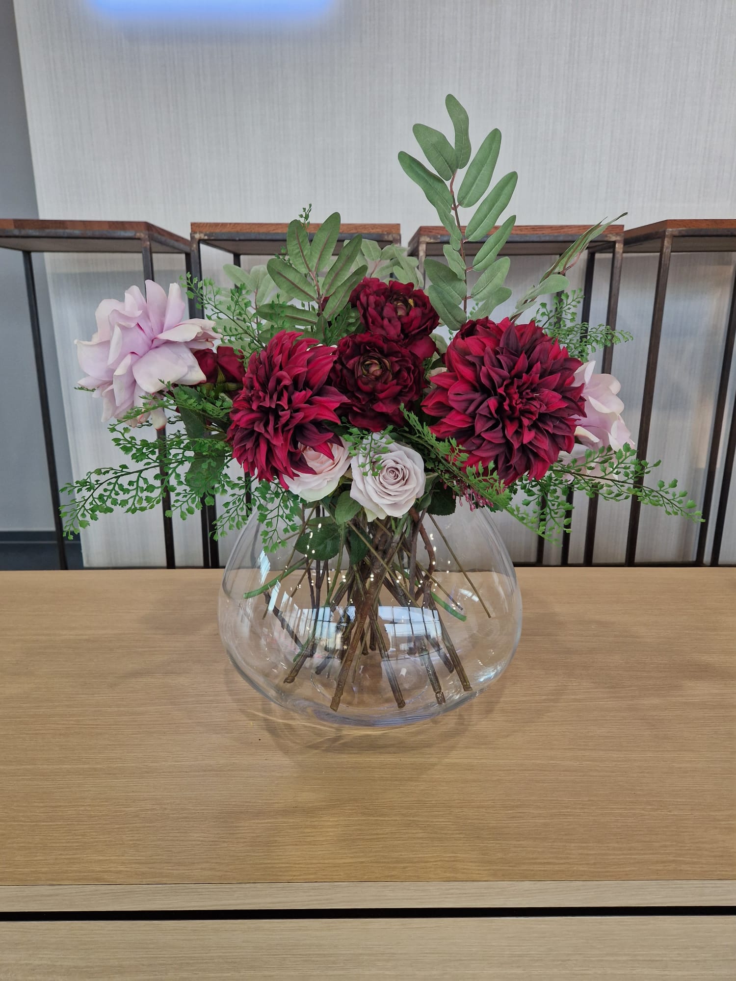 Flower arrangement of pink, red, and white blooms in a clear glass vase on a wooden table