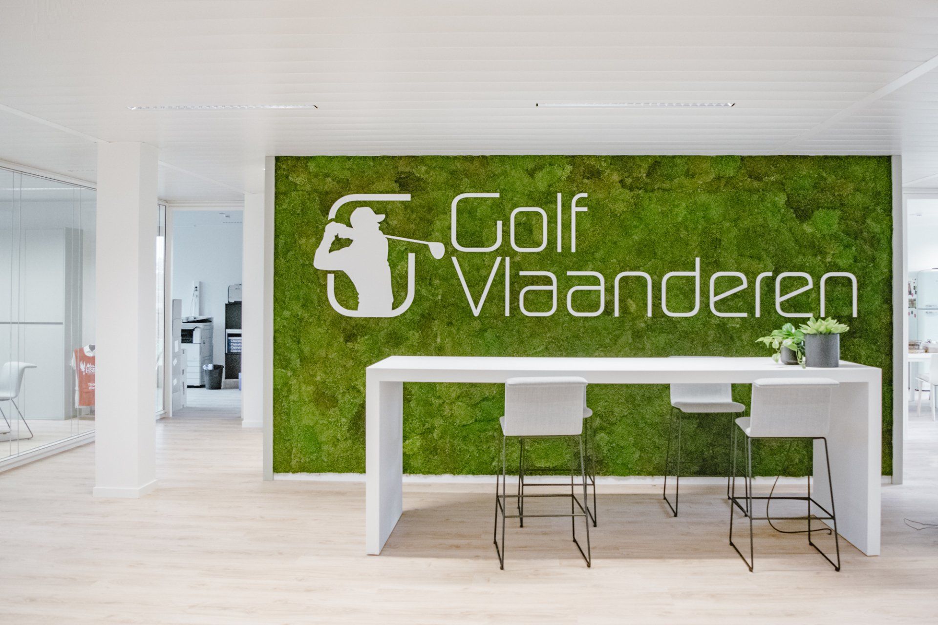 Modern office lobby with green moss wall logo reading “Golf Vlaanderen” and white reception desk