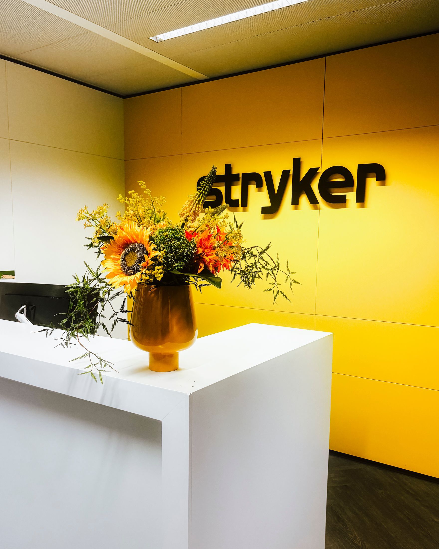 Stryker office lobby with yellow wall, white reception desk, and orange flower arrangement