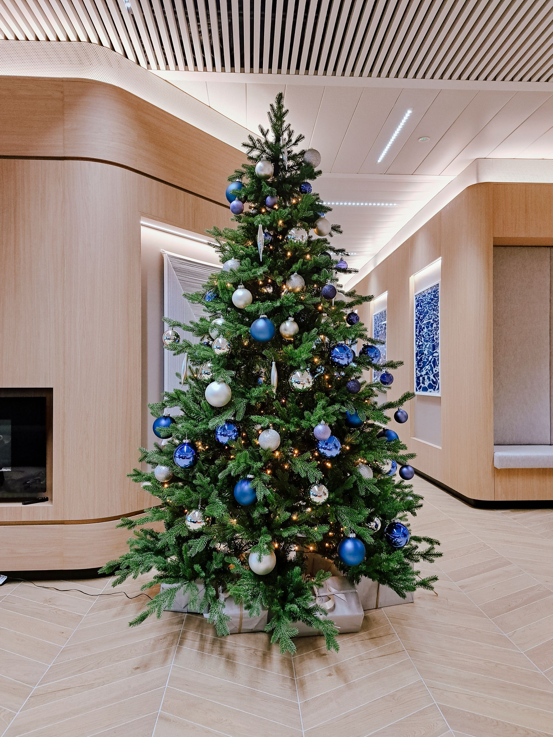 Decorated Christmas tree with blue, white, and gold ornaments in a modern lobby