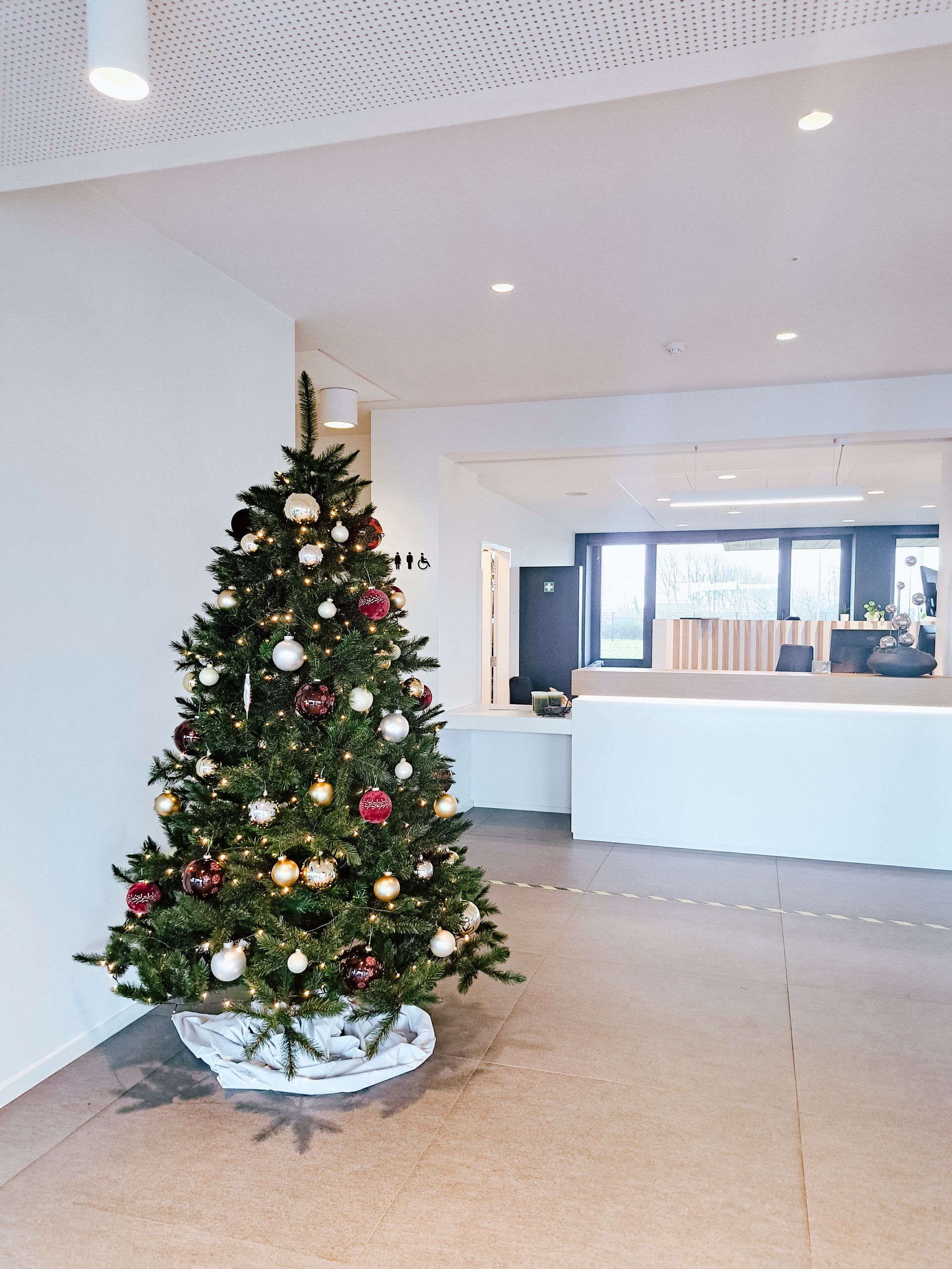 Christmas tree in a bright lobby with a white reception desk and tiled floor