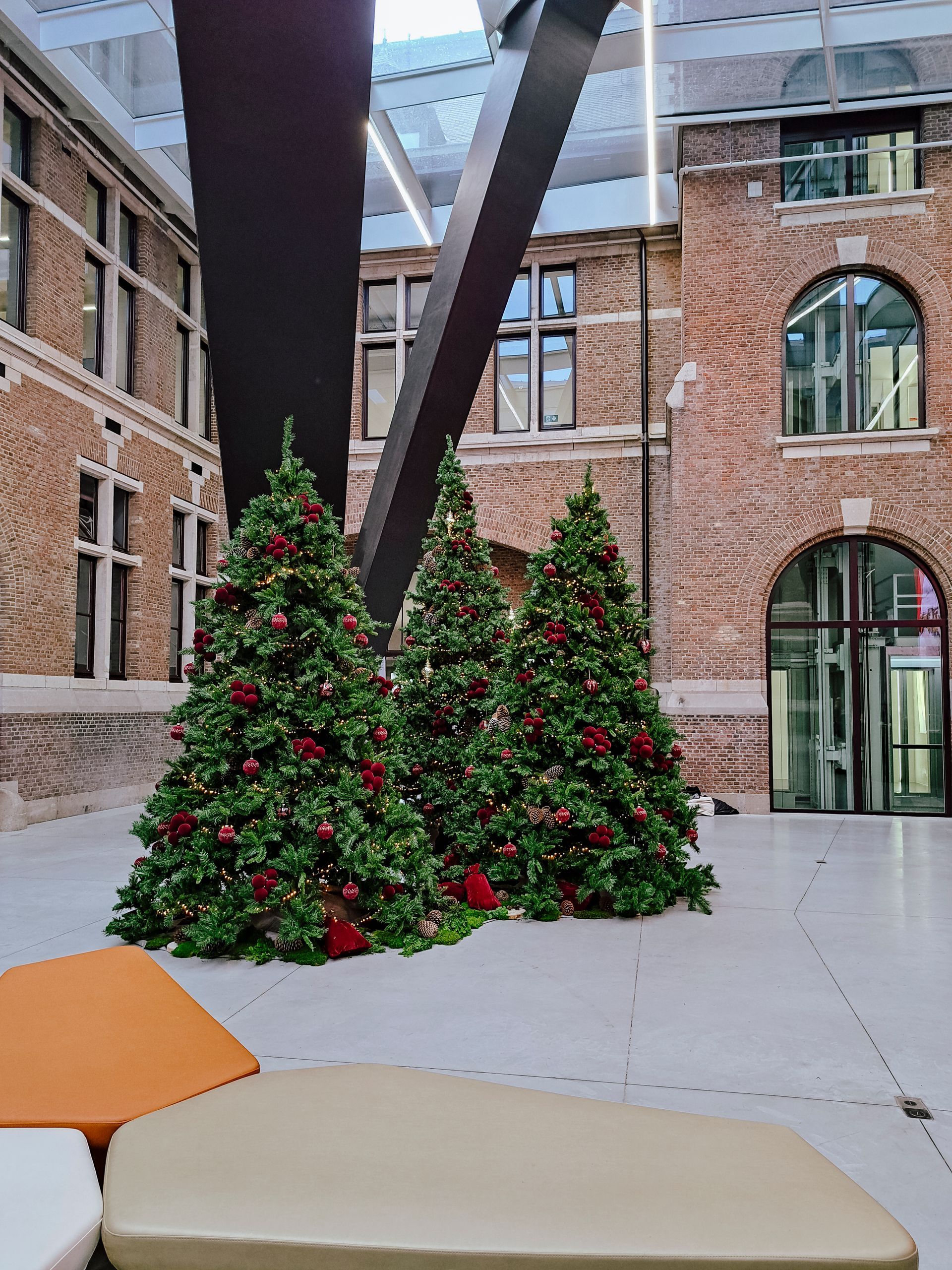 Two decorated Christmas trees in a brick courtyard with arched windows and large steel beams