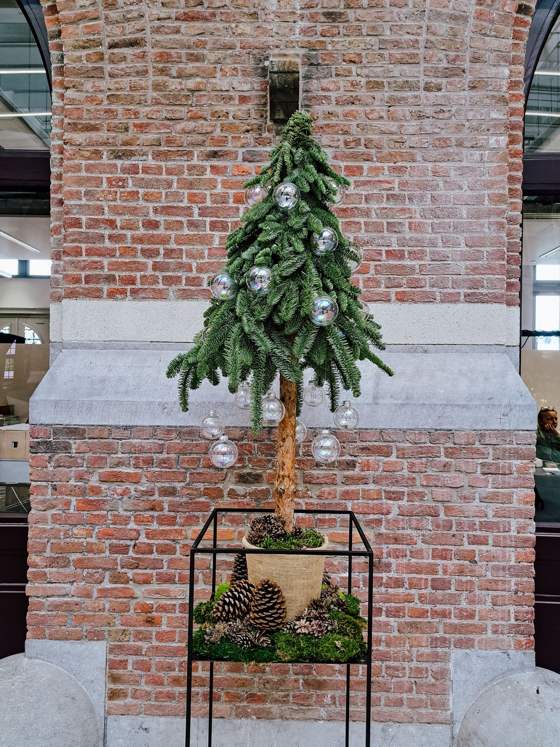 Small potted tree sculpture in front of a brick wall with a gray horizontal band