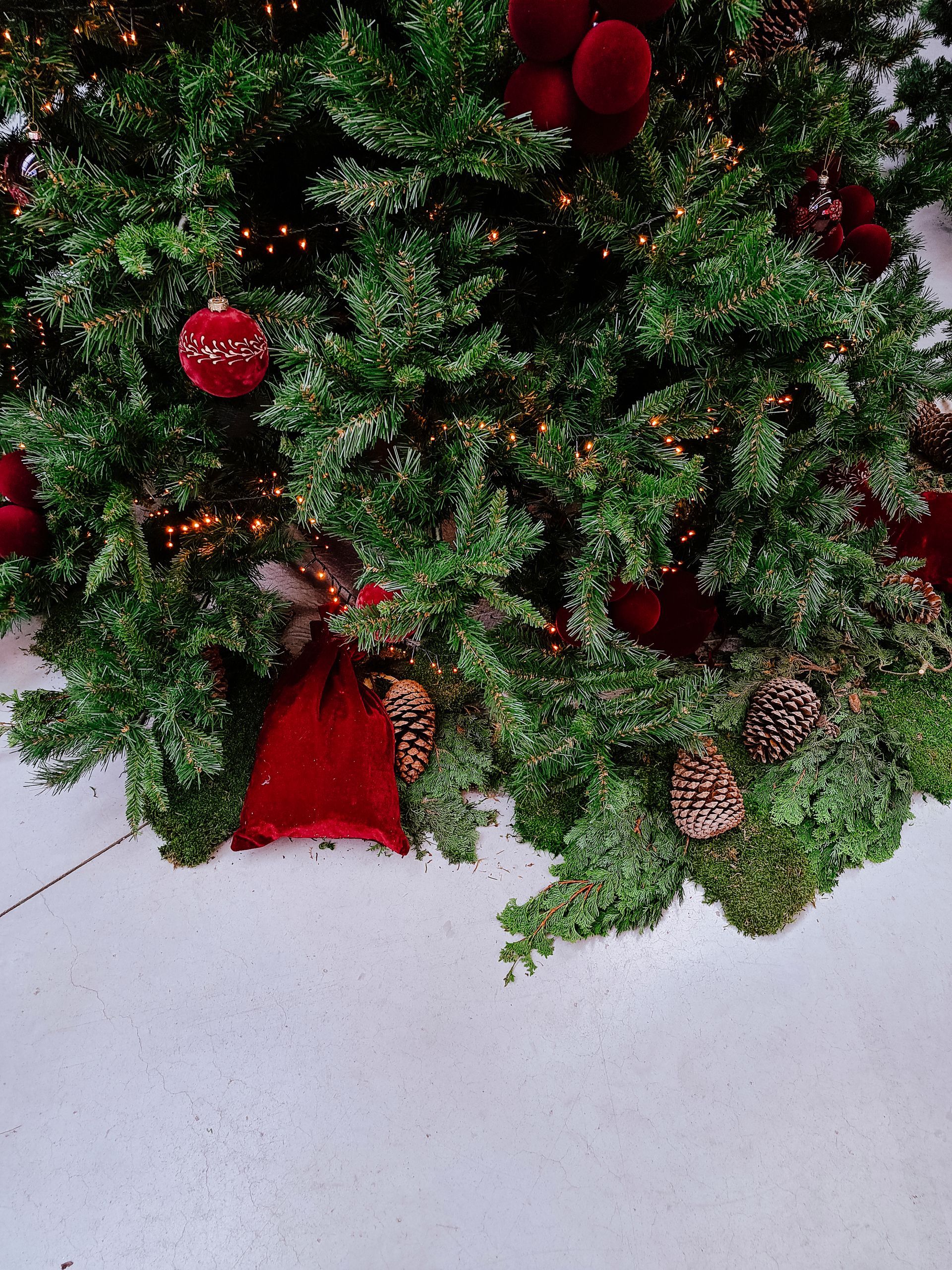 Decorated Christmas tree with red ornaments and pinecones on a white floor
